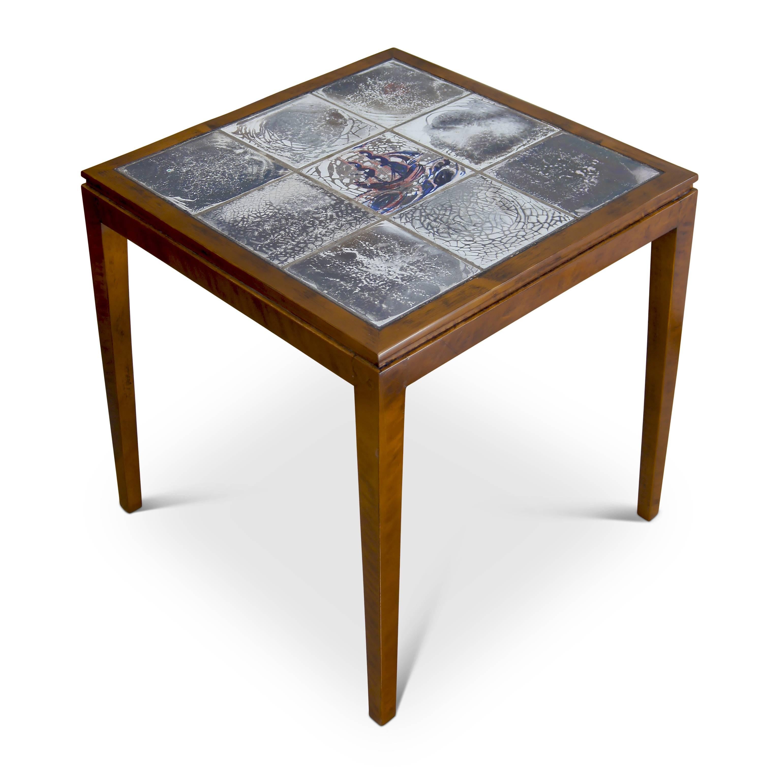 Occasional table designed and executed by Frits Henningsen, with square top and four tapered legs in beech, and having a very handsome inset tile top with atmospheric craquelure luster glazes and central ship motif designed and painted by Jens