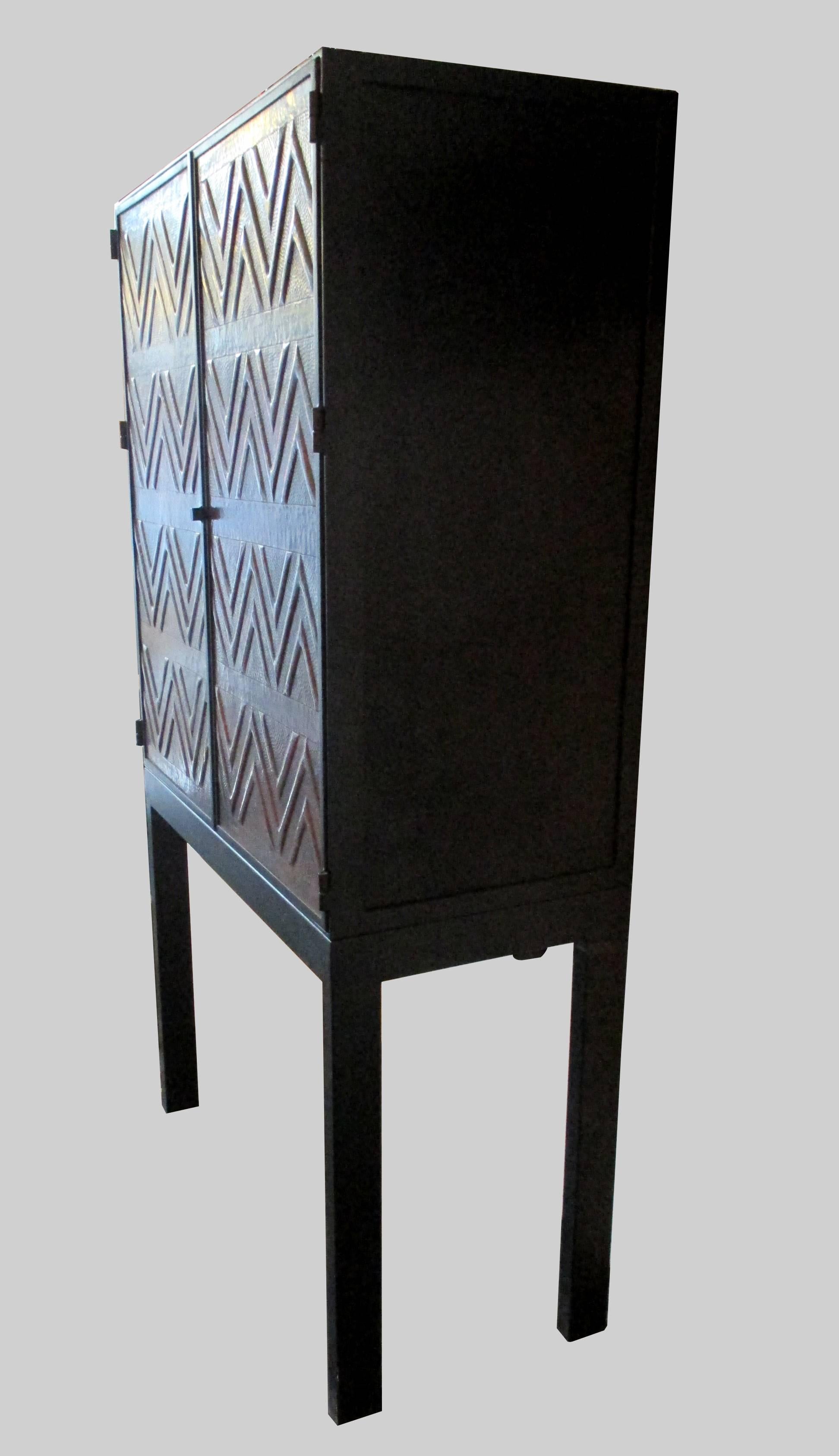 A tall cabinet in steel with masterfully crafted copper doors. The interior is in mirror and glass. Also it includes led lighting on the inside when the doors are opened.