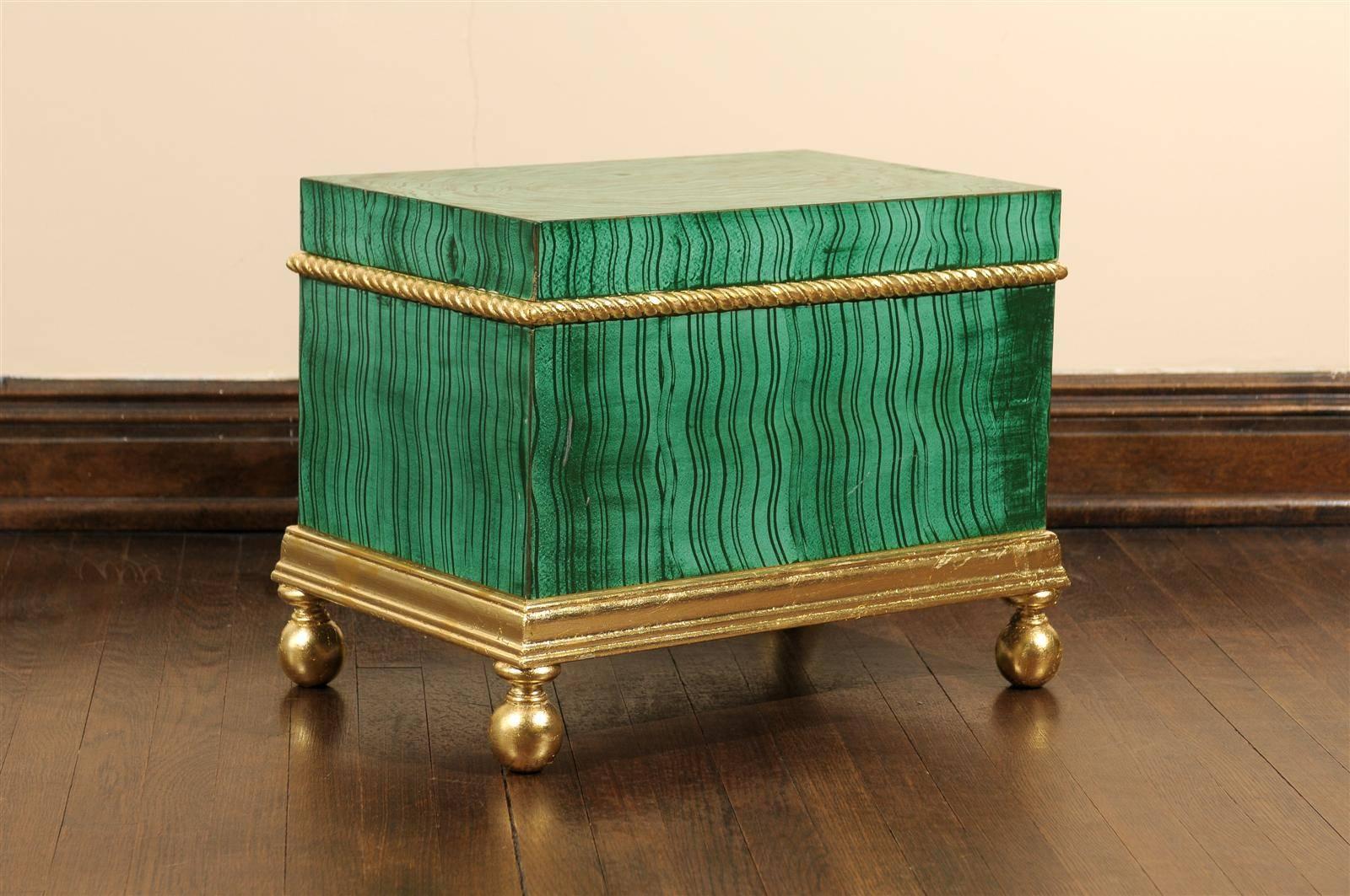 Hollywood Regency wooden chest or trunk hand-painted in a faux malachite design with gold leaf piping beneath a removable lid and raised on a gold leaf stand with bun feet.