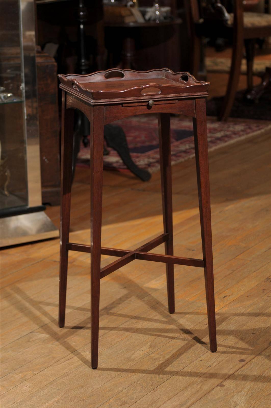 20th century square mahogany side or drinks table with a scalloped gallery tray over an arched frieze holding one candle slide with a brass knob. The table rests on square tapered legs, joined by an X-stretcher.