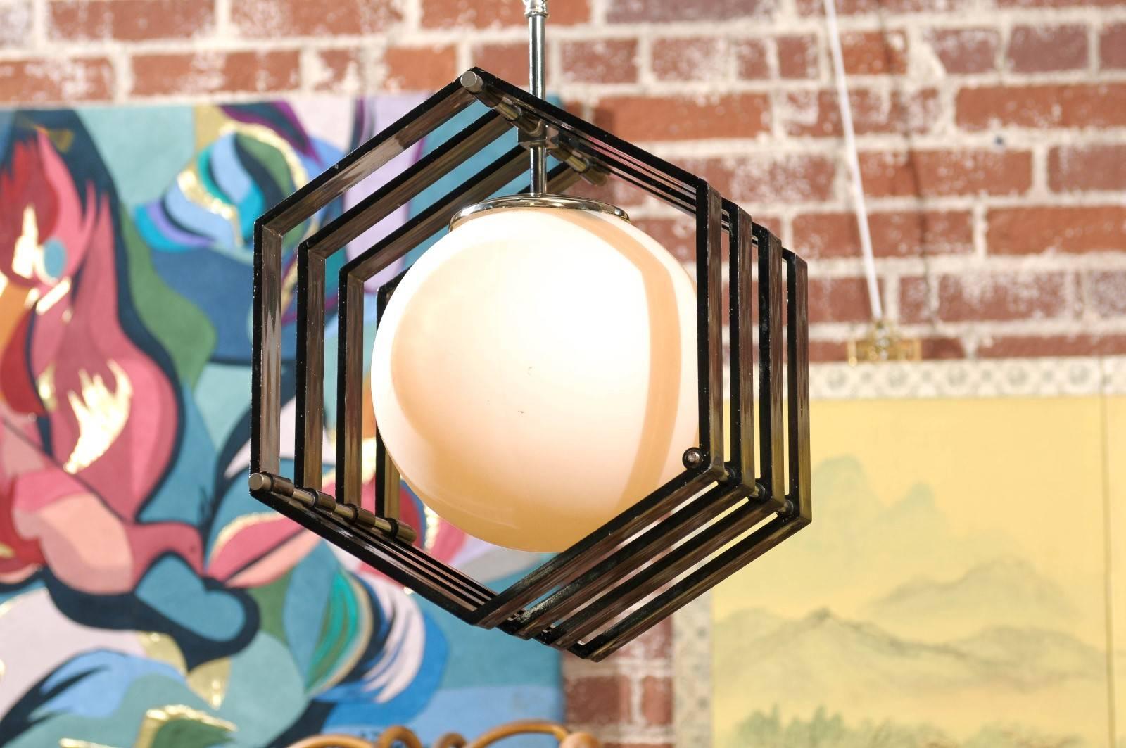 Mid-Century Modern pendant having chrome hardware and a white glass globe suspended from a hexagonal four band frame of dark blue gray acrylic.