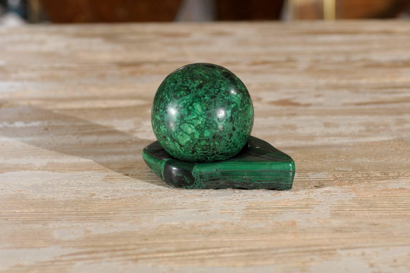 A paperweight or desk accessory in two parts made of solid malachite. The upper is a near round polished ball and it rests on a polished base hallowed slightly to hold it securely.