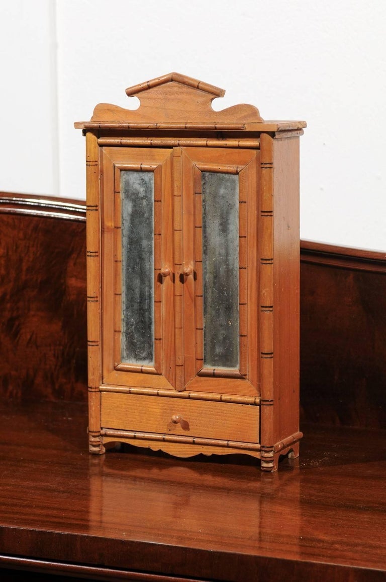 19th century French miniature armoire or wardrobe made from faux bamboo with a pair of mirrored doors and one drawer. The piece bares the label of the Bazar de l'Hôtel de Ville, a 19th century Parisian department store.