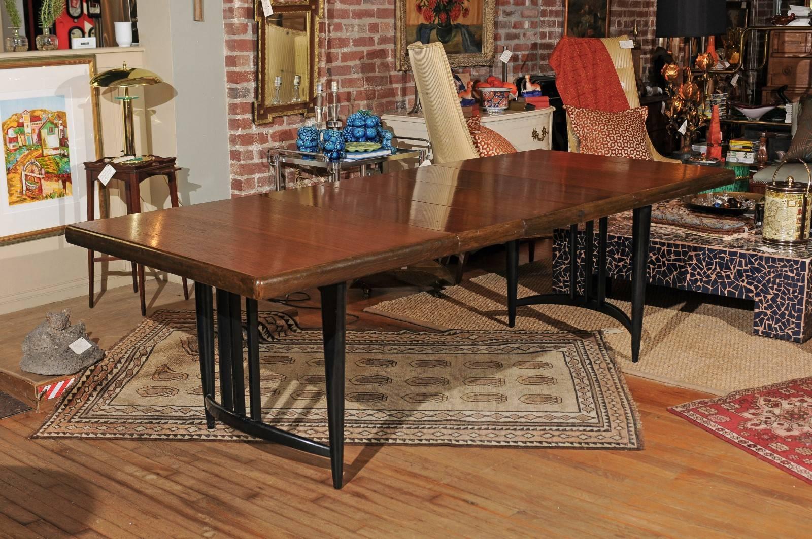 Mid-20th Century dining or conference room table of walnut with black lacquered legs and arched stretchers. The 58 inch wide table has three 12 inch wide leaves that can be added as needed for a maximum width of 94 inches. A set of six coordinating