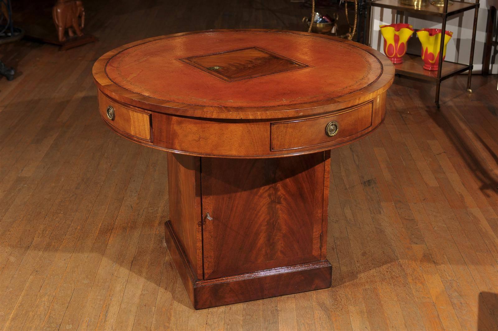 A 19th century English rent or gaming table created in the Georgian style. The table has a tooled leather drum shaped top in a lovely shade of naturally faded red. The revolving table top contains a central till constructed of flame mahogany and a