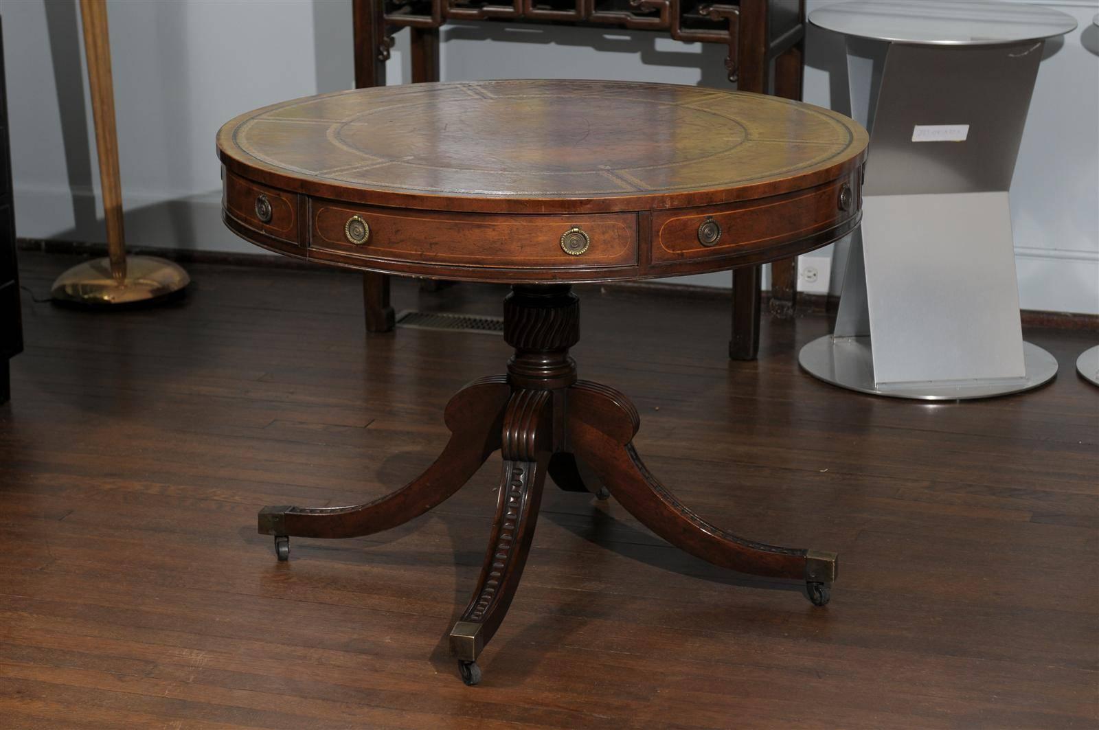 20th century Georgian style drum or rent table by Baker Furniture Company. The table features the original inset and embossed brown leather top. The table's mahogany veneered frieze holds two drawers and four faux drawers with molded edges and brass