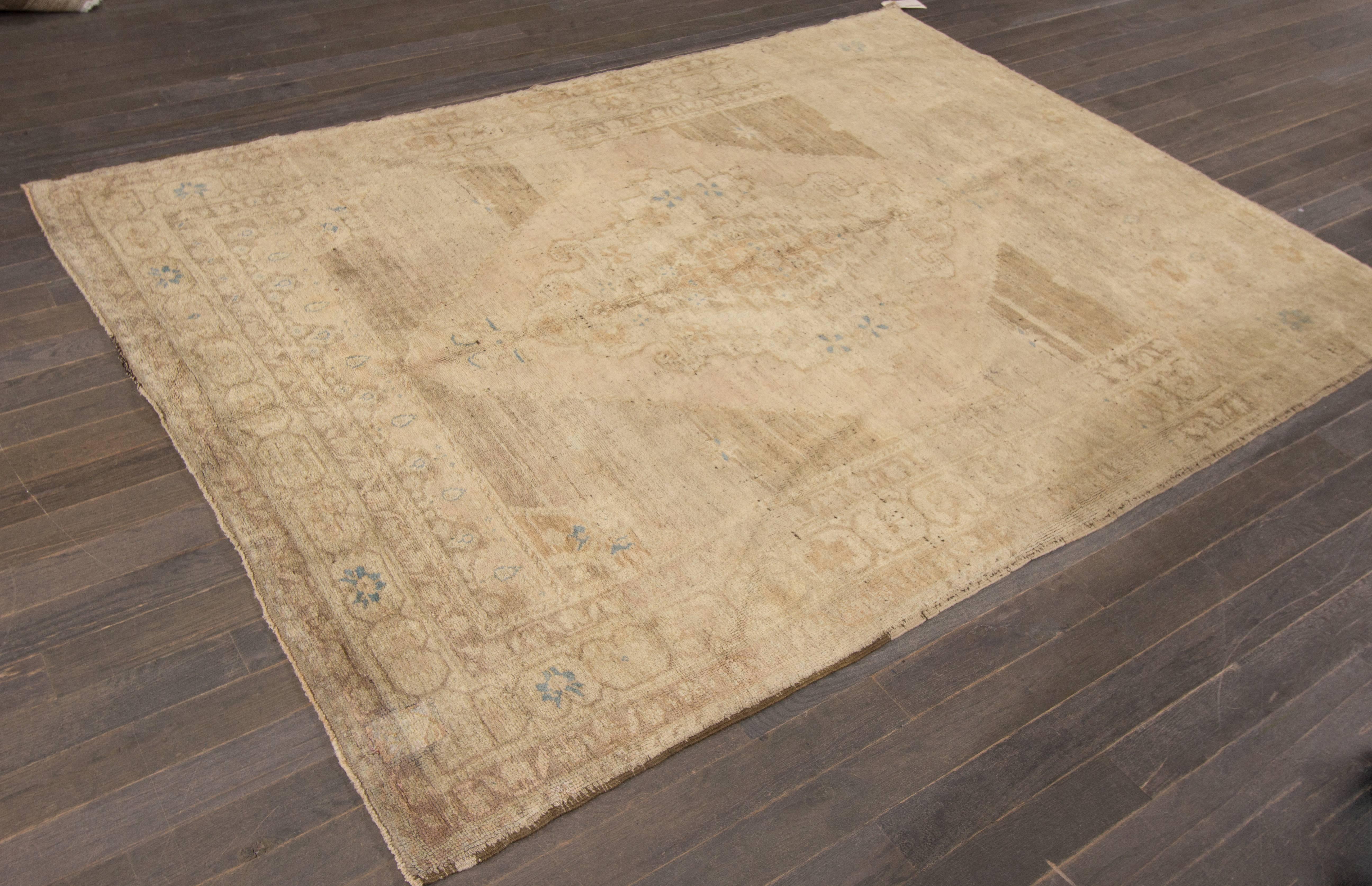 20th century Turkish Khotan-style carpet. Features a beige and tan field surrounding a traditional, central medallion design with blue accents. Measures approximately 5 feet 7 inches by 7 feet 7 inches.