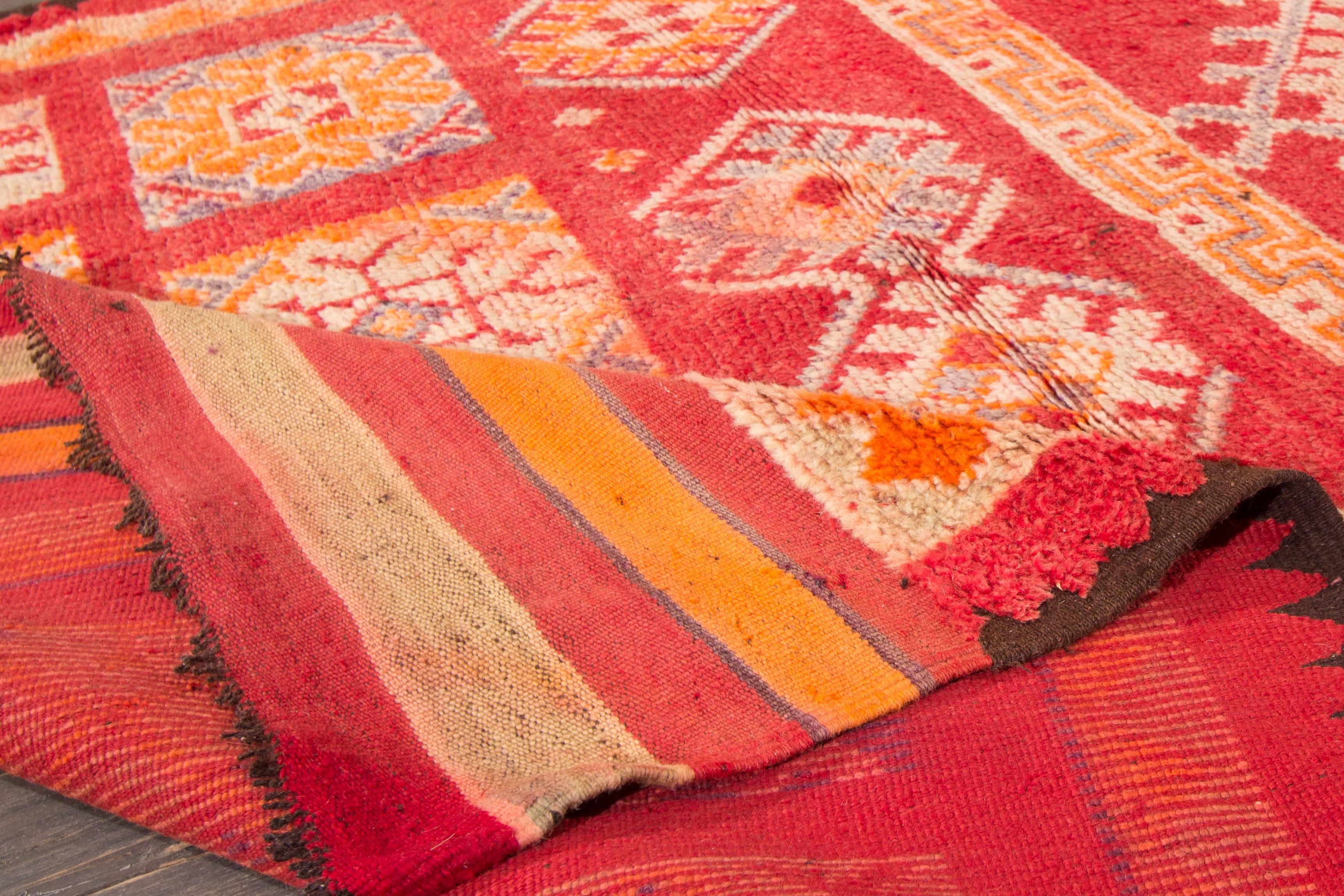 Vintage 1945 Moroccan rug with a bright red field and geometric designs in orange and blue tones. Measures 5.10x13.02.