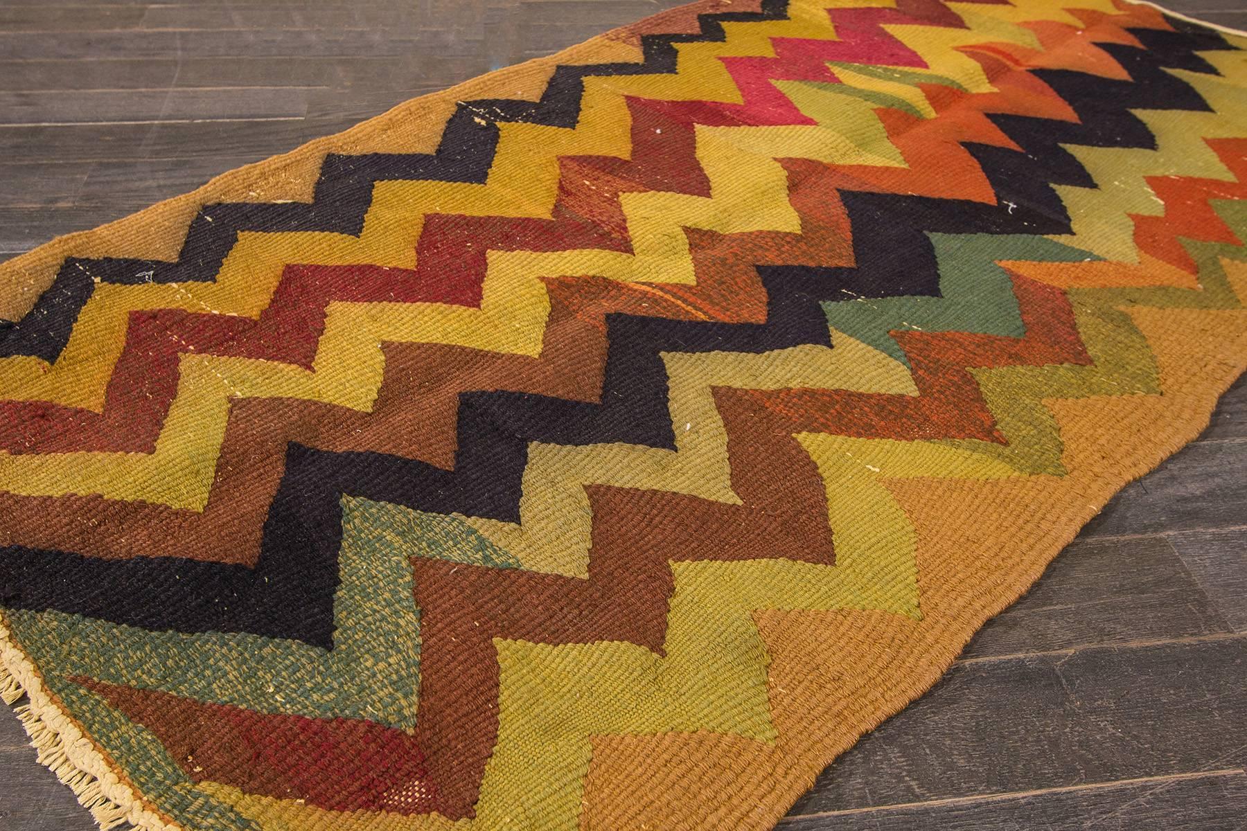 A handwoven Turkish Kilim rug with a geometric stripe pattern. Accents of yellow, black, blue, green and orange throughout.