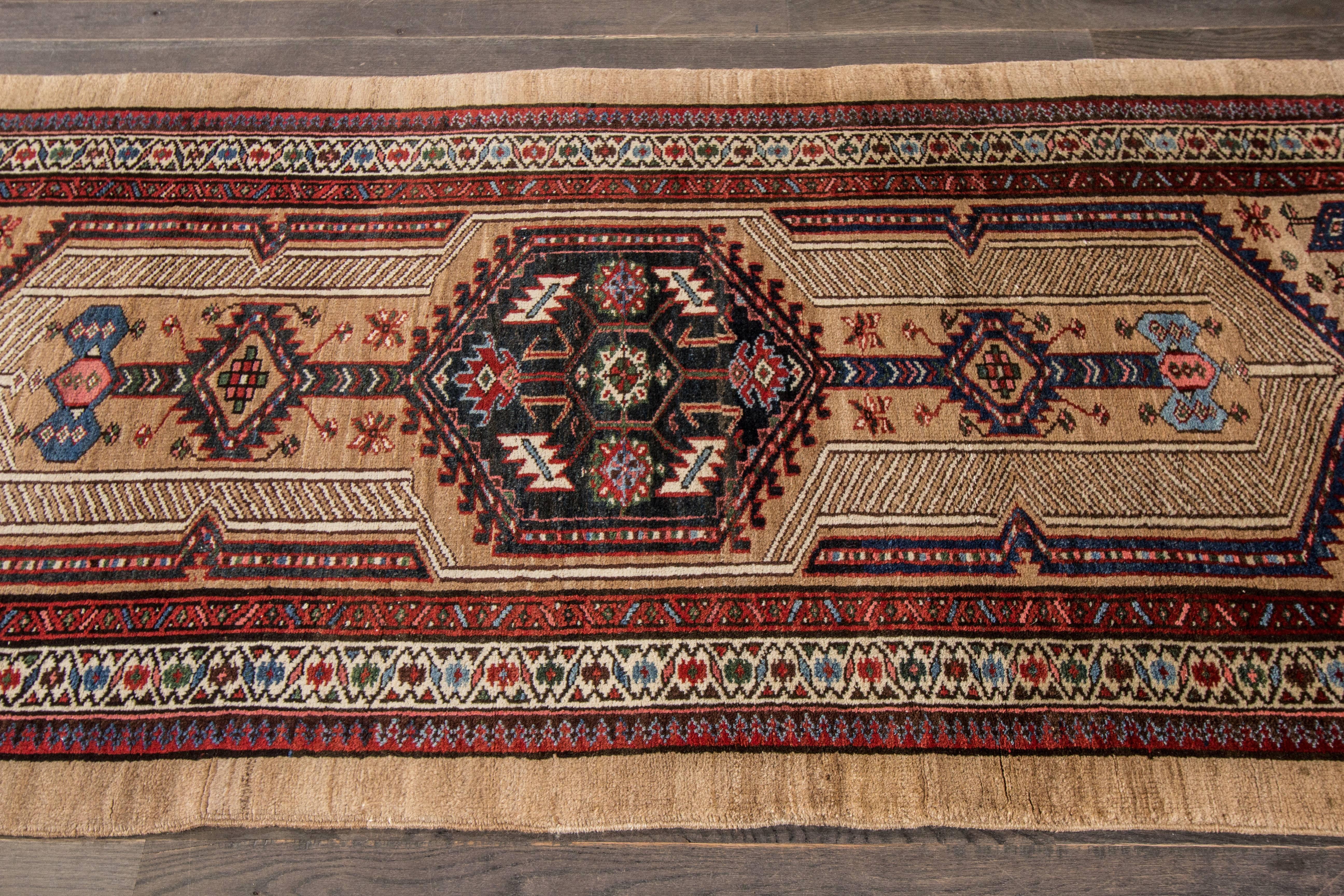 Measures: 3'.3 x 7'.5
A hand-knotted antique Persian Serab rug with a geometric floral design on a beige field. Accents of red, blue and ivory throughout the piece.