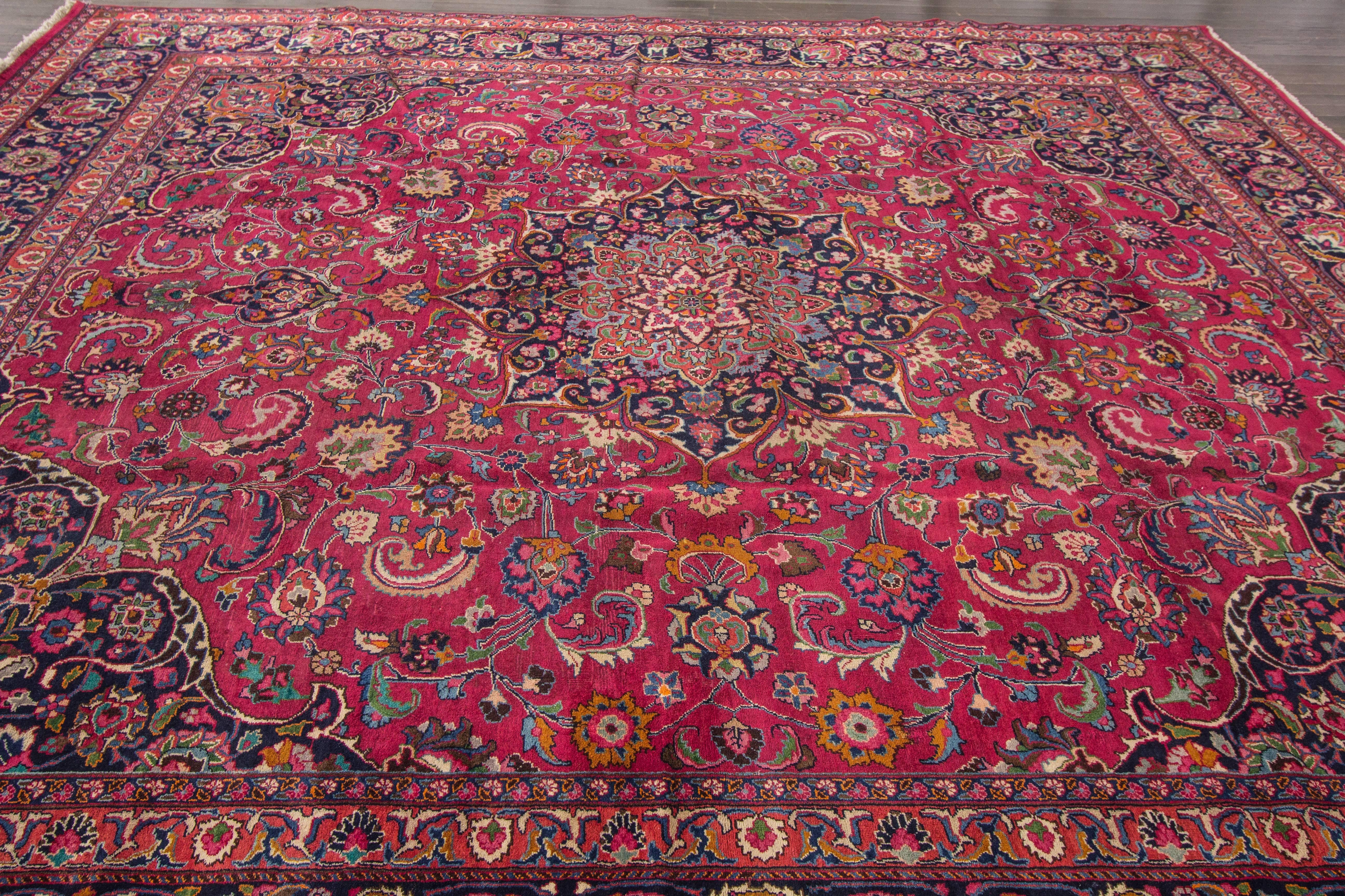 A hand-knotted vintage Mashad rug with a floral medallion design on a red field. Accents of brown, yellow, blue and ivory throughout the piece. This piece is 11'.7 x 12'.7.