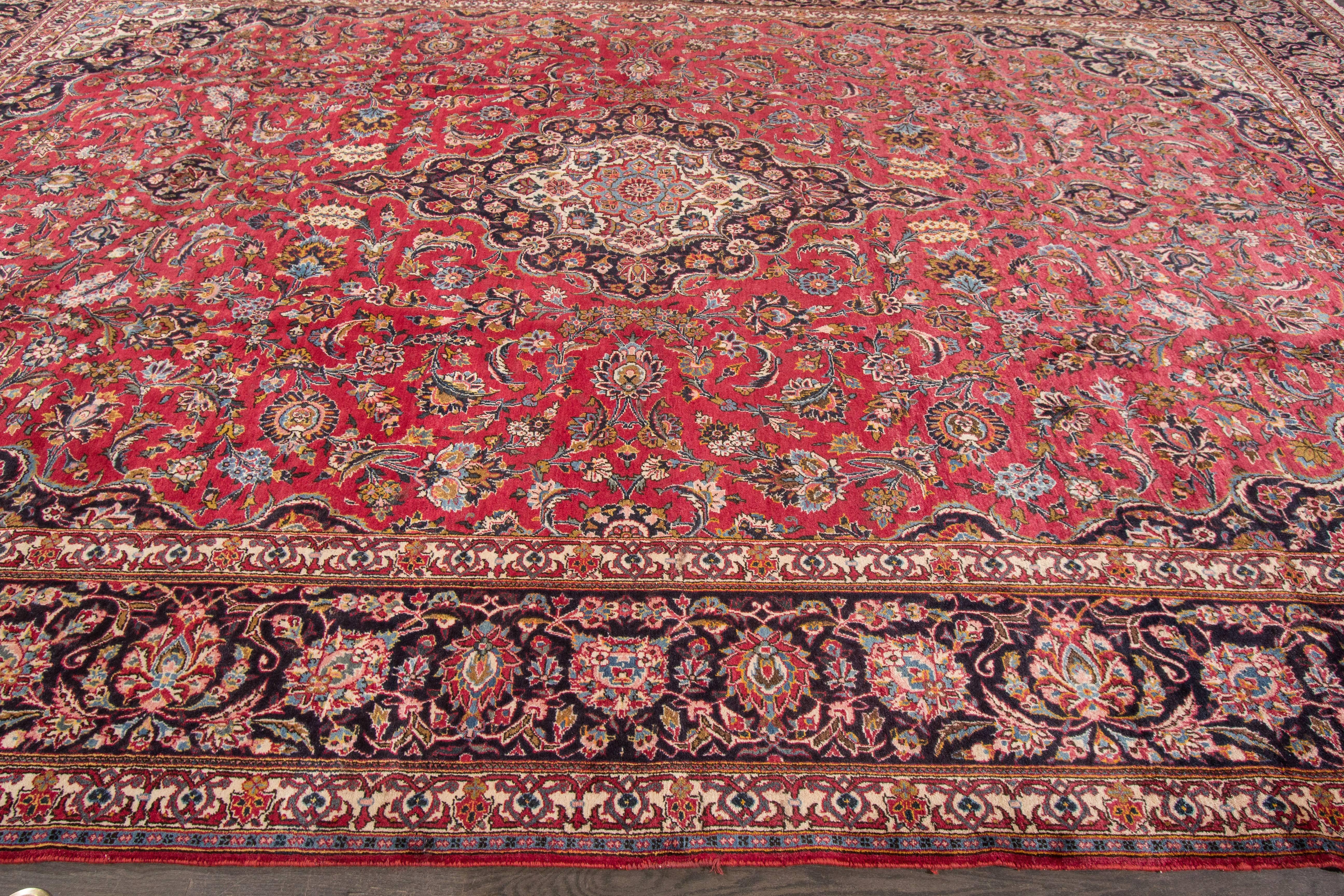 A hand-knotted vintage Kashan rug with a floral medallion design on a red field. Accents of black, blue and ivory throughout the piece. The size of this piece is 10'9 x 16'7.