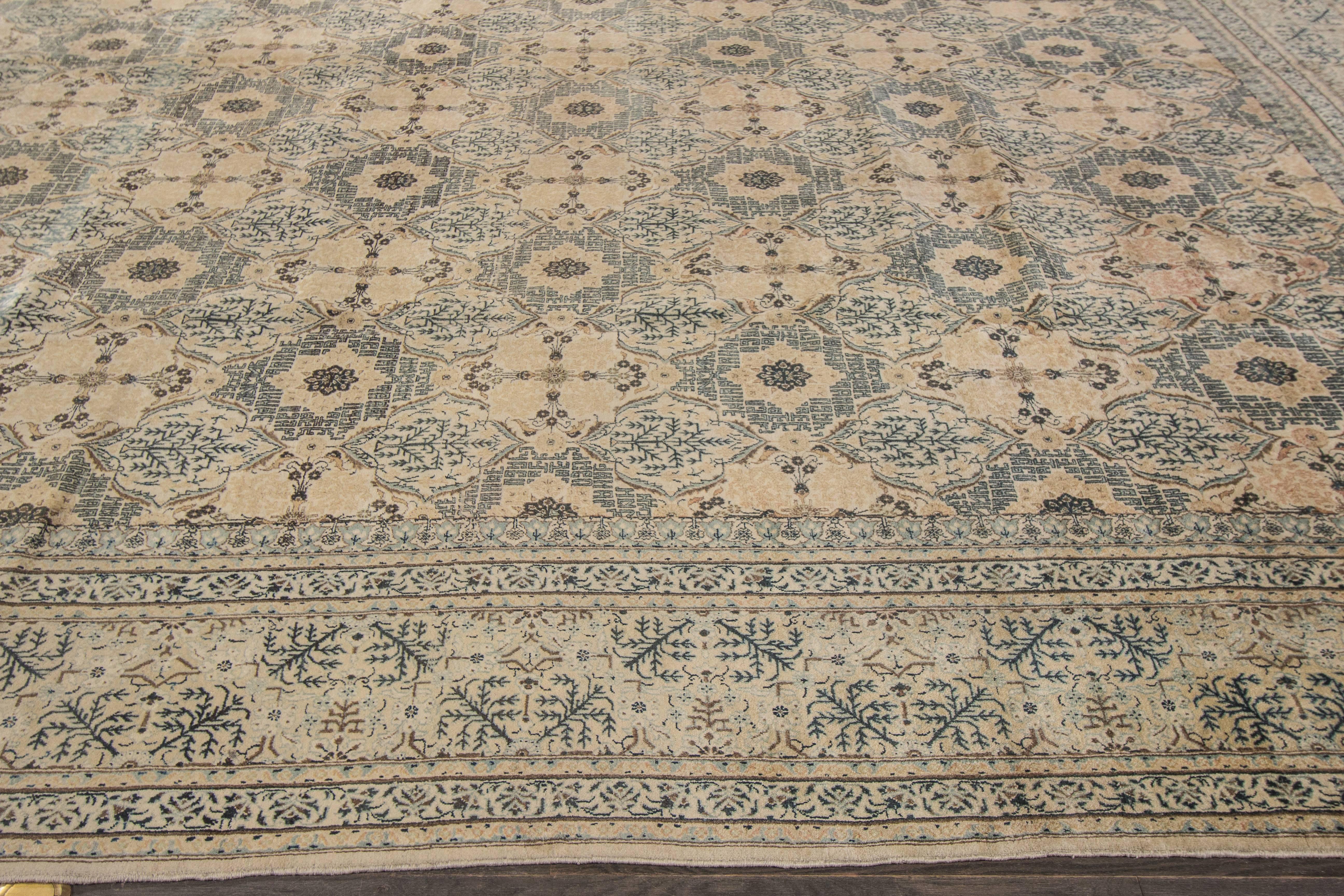 A hand-knotted antique Kashan rug with a floral pattern design on a beige field. Accents of green and brown throughout the piece. The size of this piece is 10'.6 x 14'.