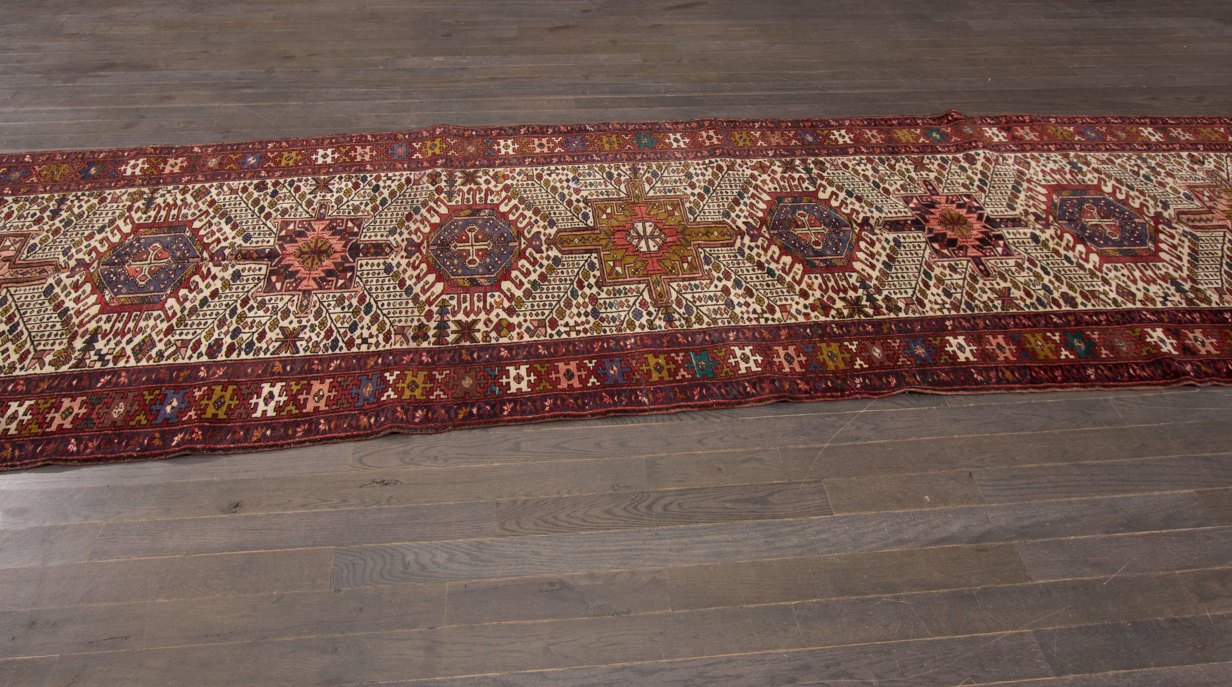 A hand-knotted antique Heriz runner with a geometric design on a red field. Accents of ivory, yellow, blue and green throughout the piece. The size of this piece is 3'.10 x 13'.2.