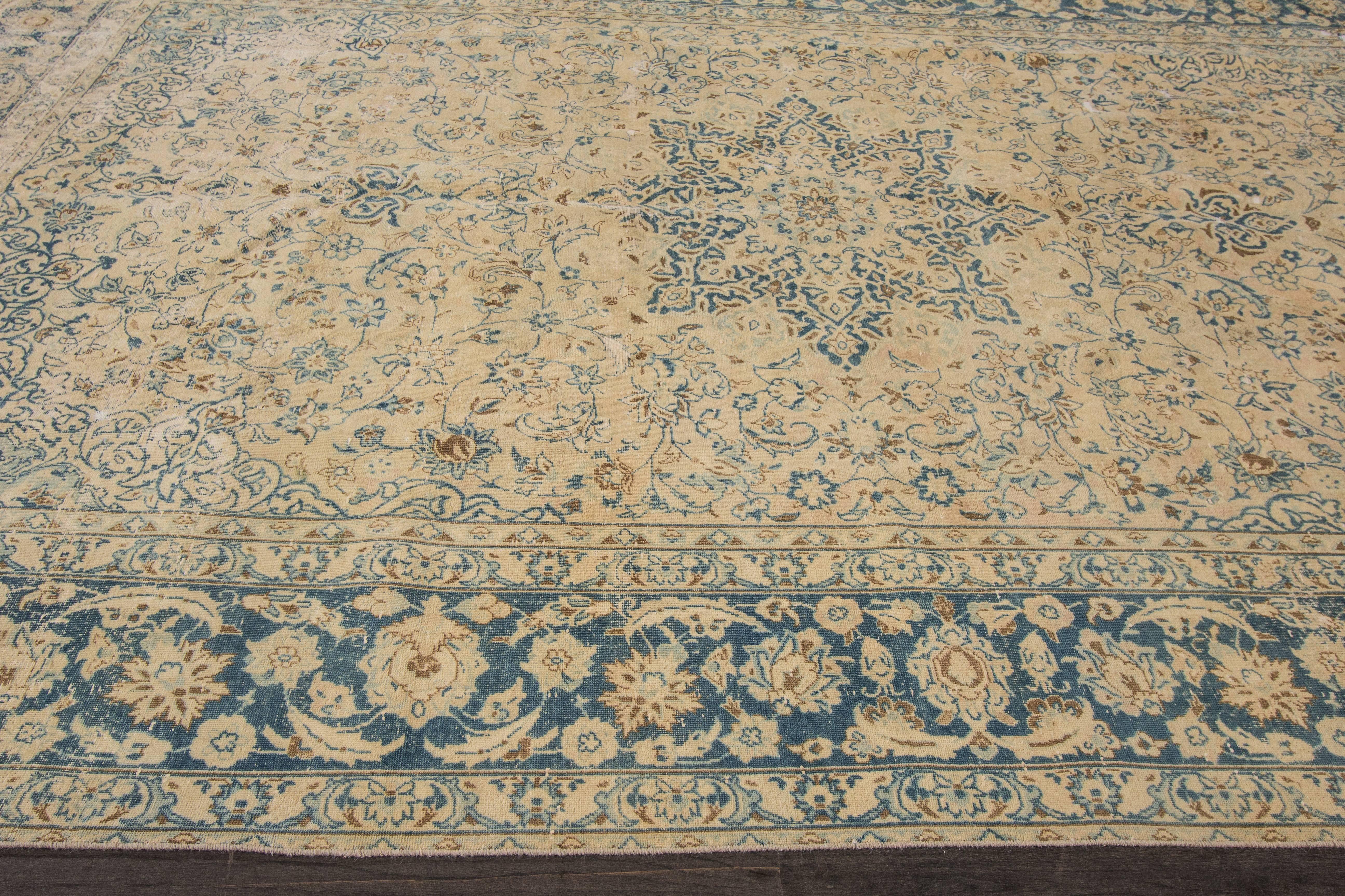 A hand-knotted vintage Persian Tabriz rug with a floral medallion design on a beige field. Accents of blue, red and brown throughout the piece. The size of this rug is 9'.3 x 13'.7.
