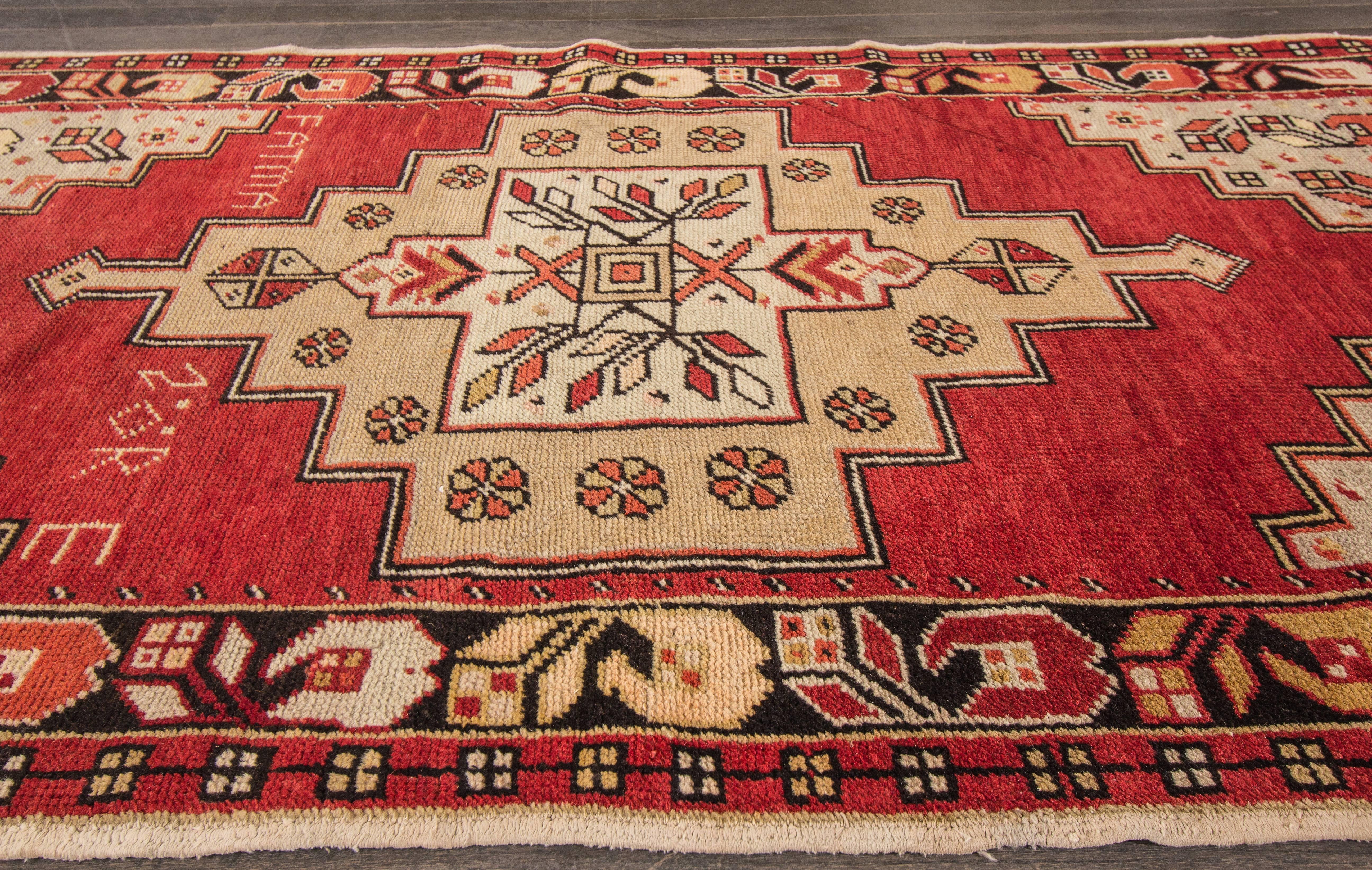 A hand-knotted Anatolian rug with a geometric design on a red field. Accents of beige, black and ivory throughout. This rug measures 3'6