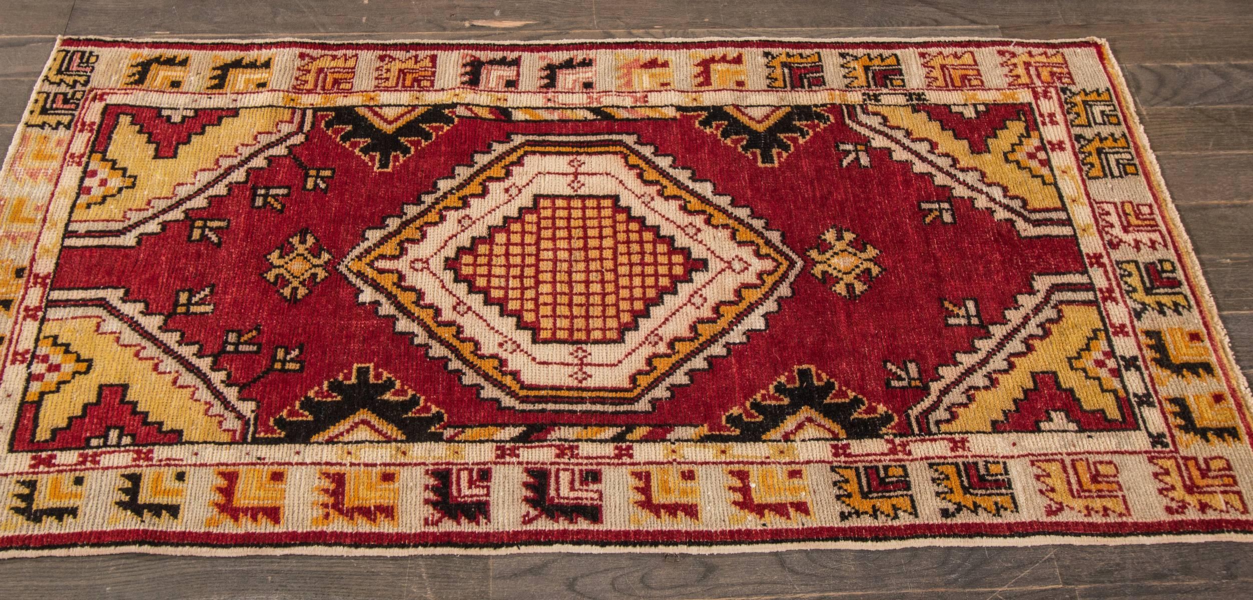 A hand-knotted vintage Anatolian rug with a geometric design on a red field. Accents of yellow, green and ivory throughout. This rug measures 2'.6 x 5'.