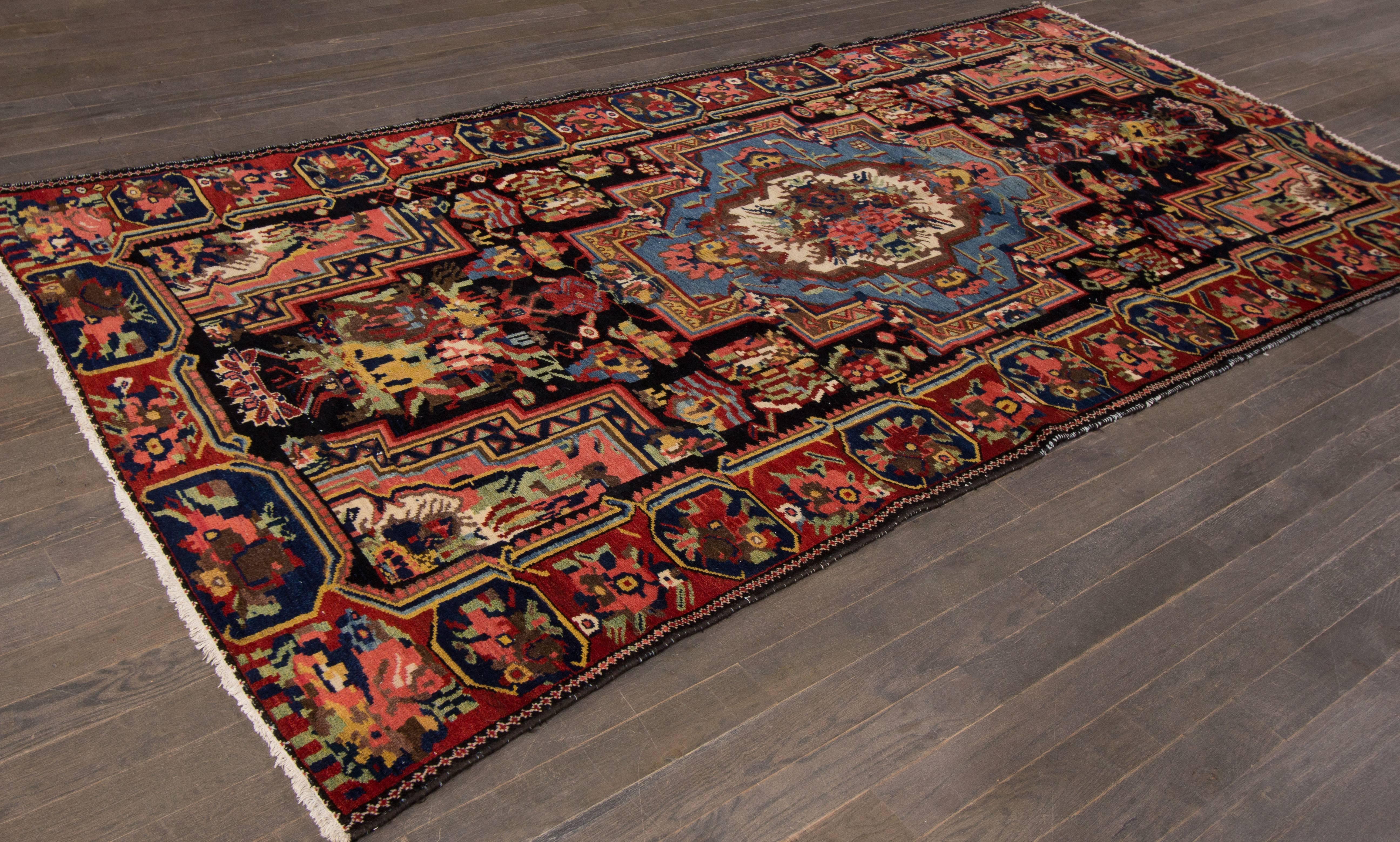 A hand-knotted vintage Bakhtiari rug with a geometric medallion design on a black field. Accents of red, brown, blue and yellow throughout the piece. This rug measures 5'.1 x 10'.4.
