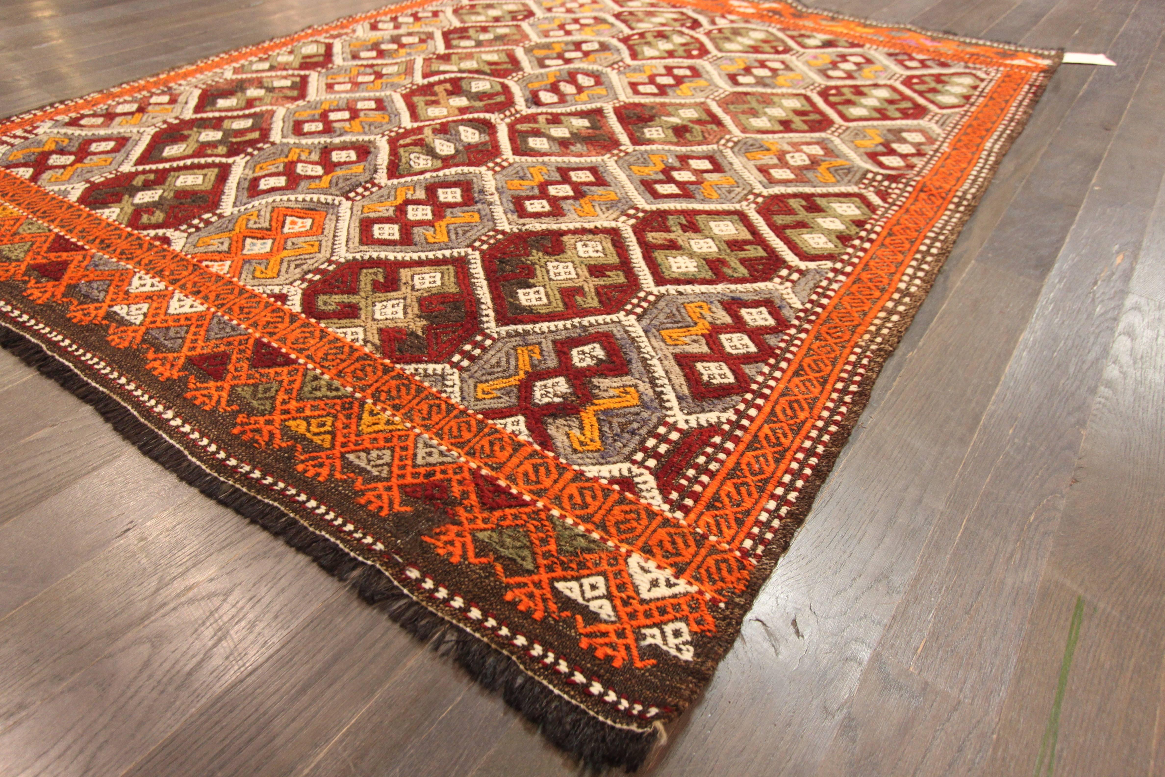 A hand-knotted Sumahk rug with a geometric pattern on a red field. Accents of orange, red and green throughout the piece. This rug measures 4'.6 x 5'.9.