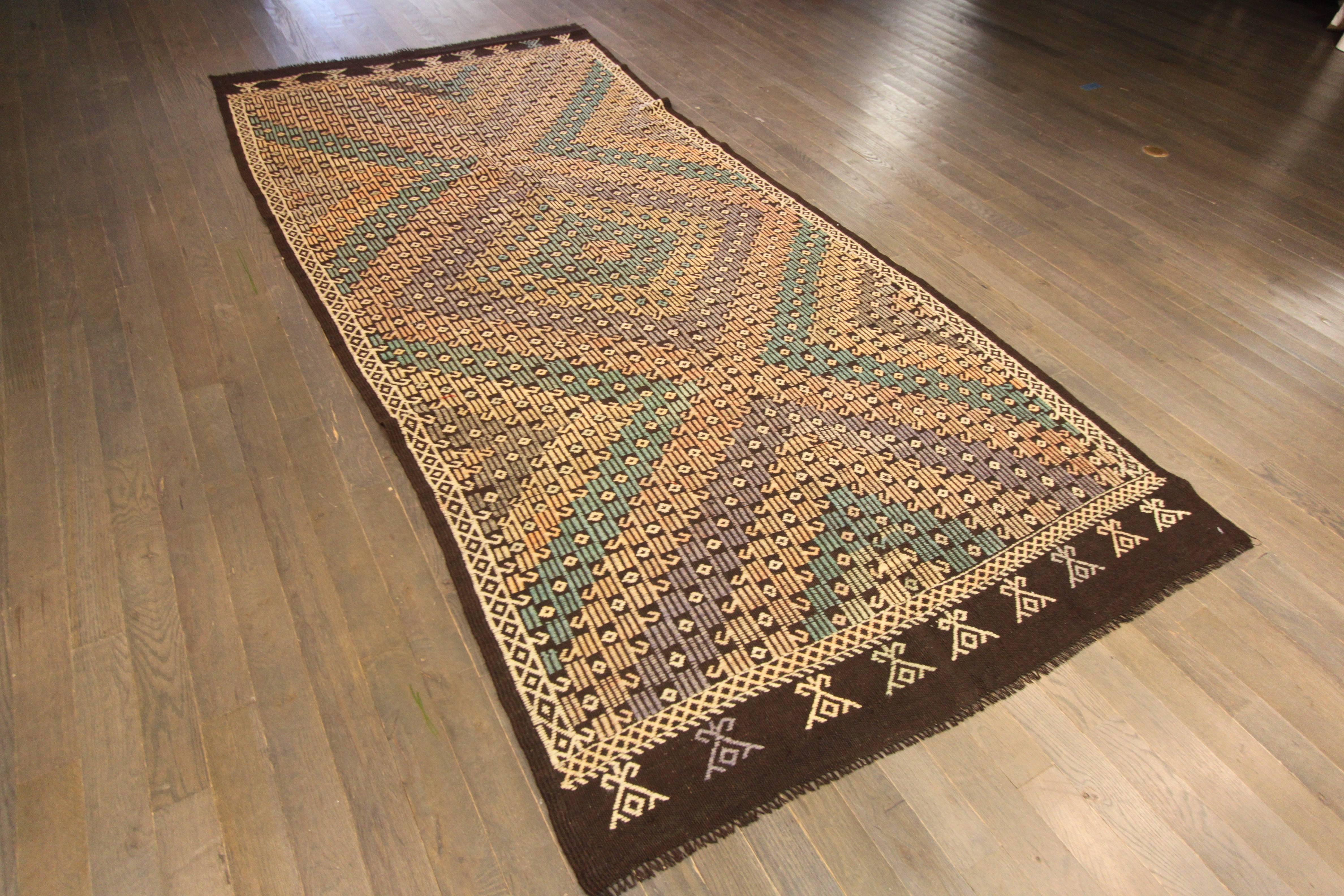 A hand-knotted Sumahk with a geometric design on a brown field. Accents of green, orange and red throughout the piece. This rug measures: 4'.10 x 10'.2.