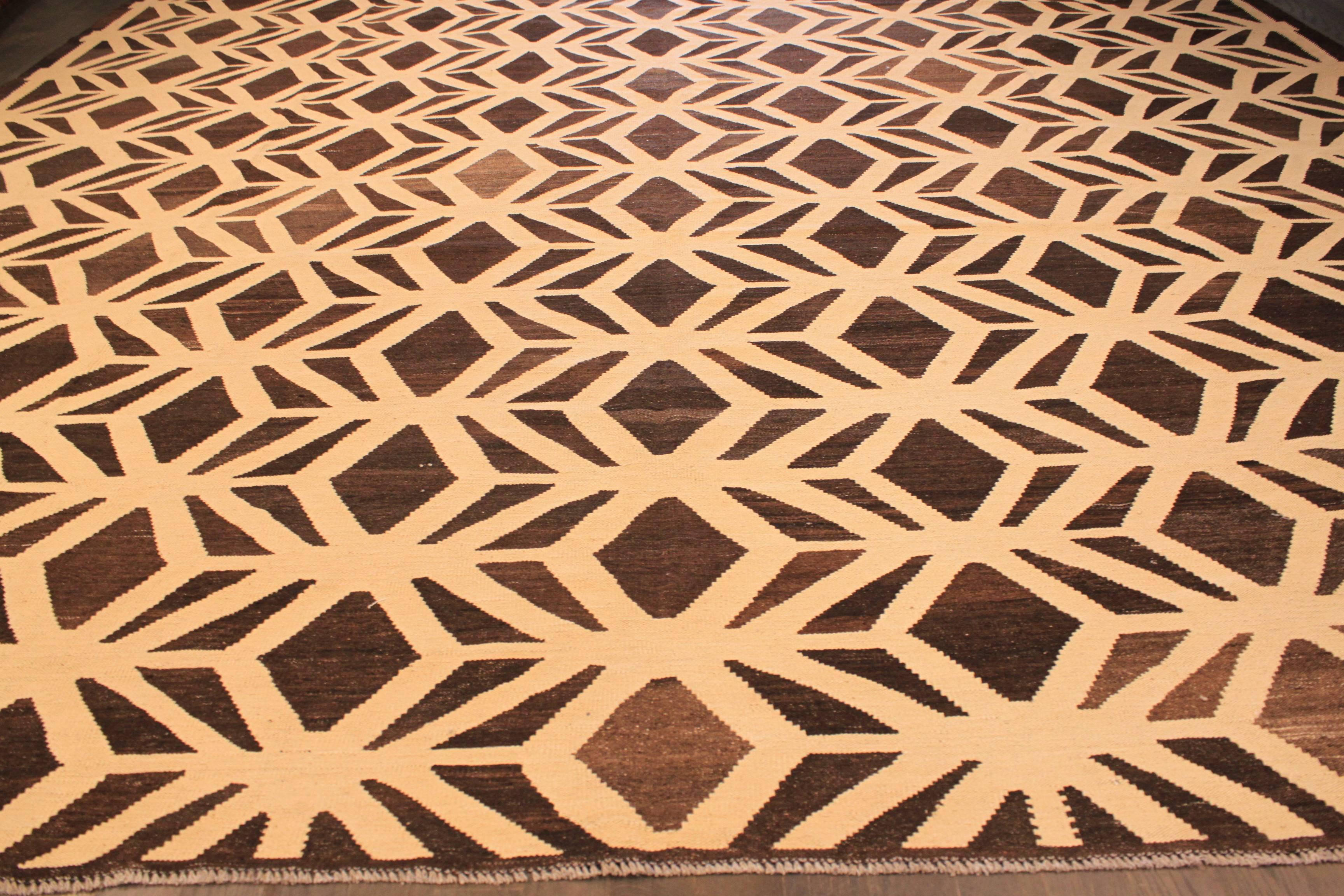 A hand-knotted Kilim rug with a geometric design on a brown field. Accents of beige and brown throughout the piece. This rug measures 12'.3 x 14'.9.