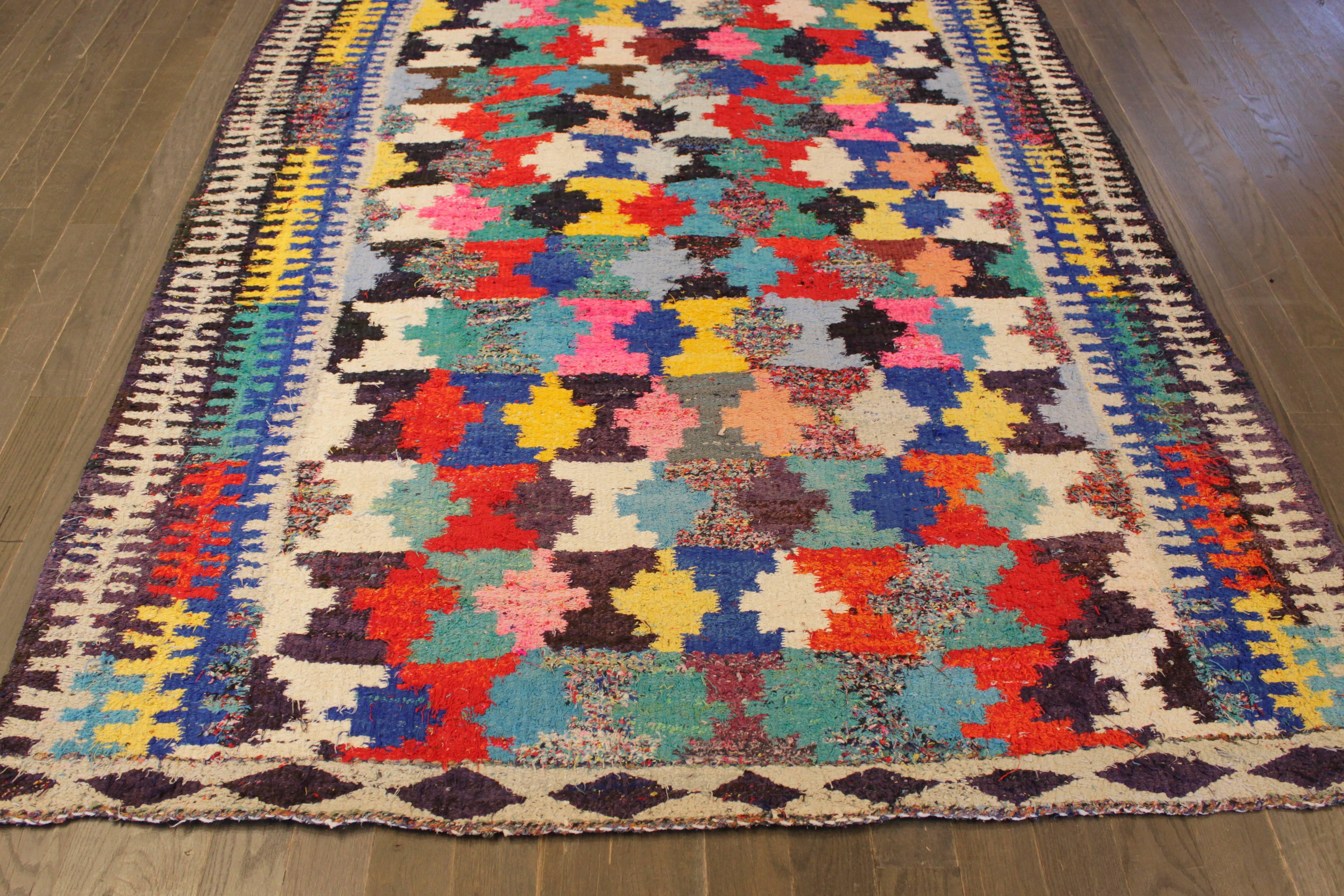 A hand-knotted Kilim rug with an artistic design on a black field. Accents of ivory, yellow, red and blue throughout the piece. This rug measures: 5'.3 x 10'.1.