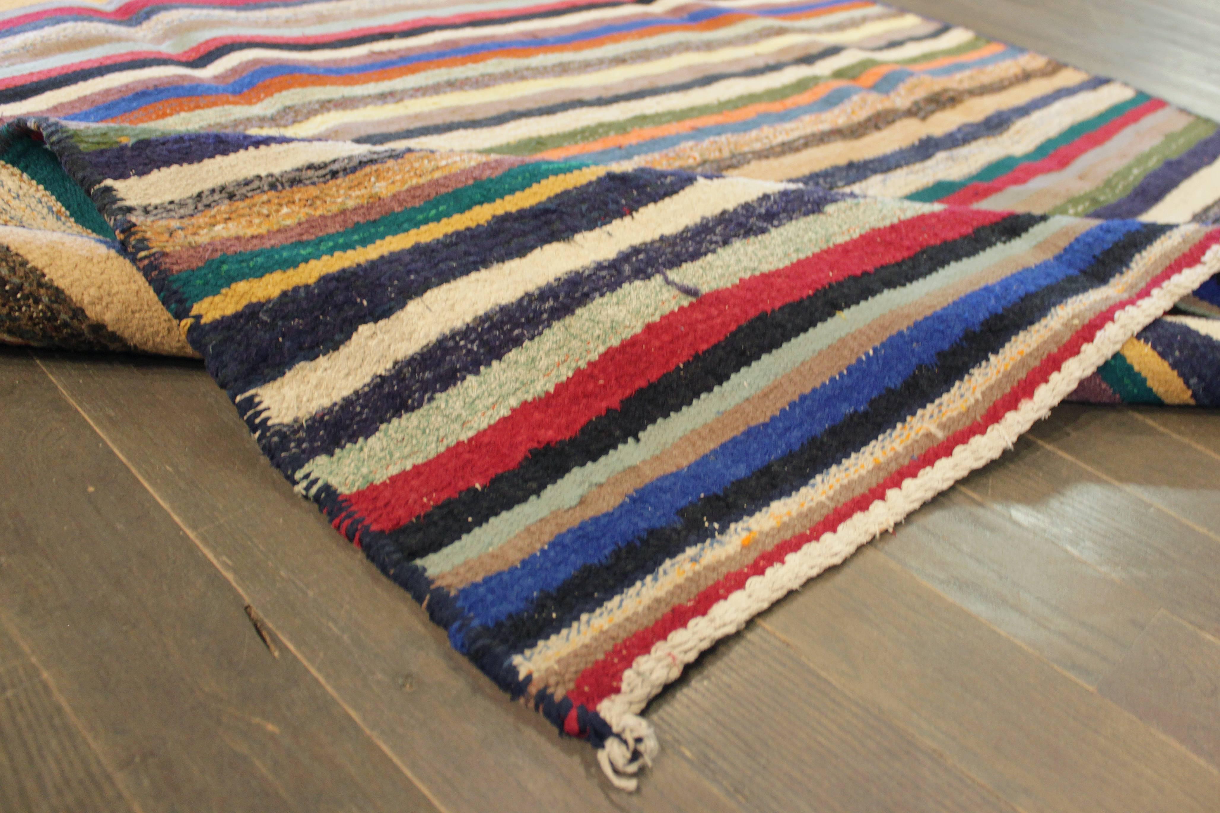 A hand-knotted Kilim rug with a stripe design on a multi-color field. Accents of blue, ivory, red, green and black throughout the piece. This rug measures: 4'.7 x 8'.7.