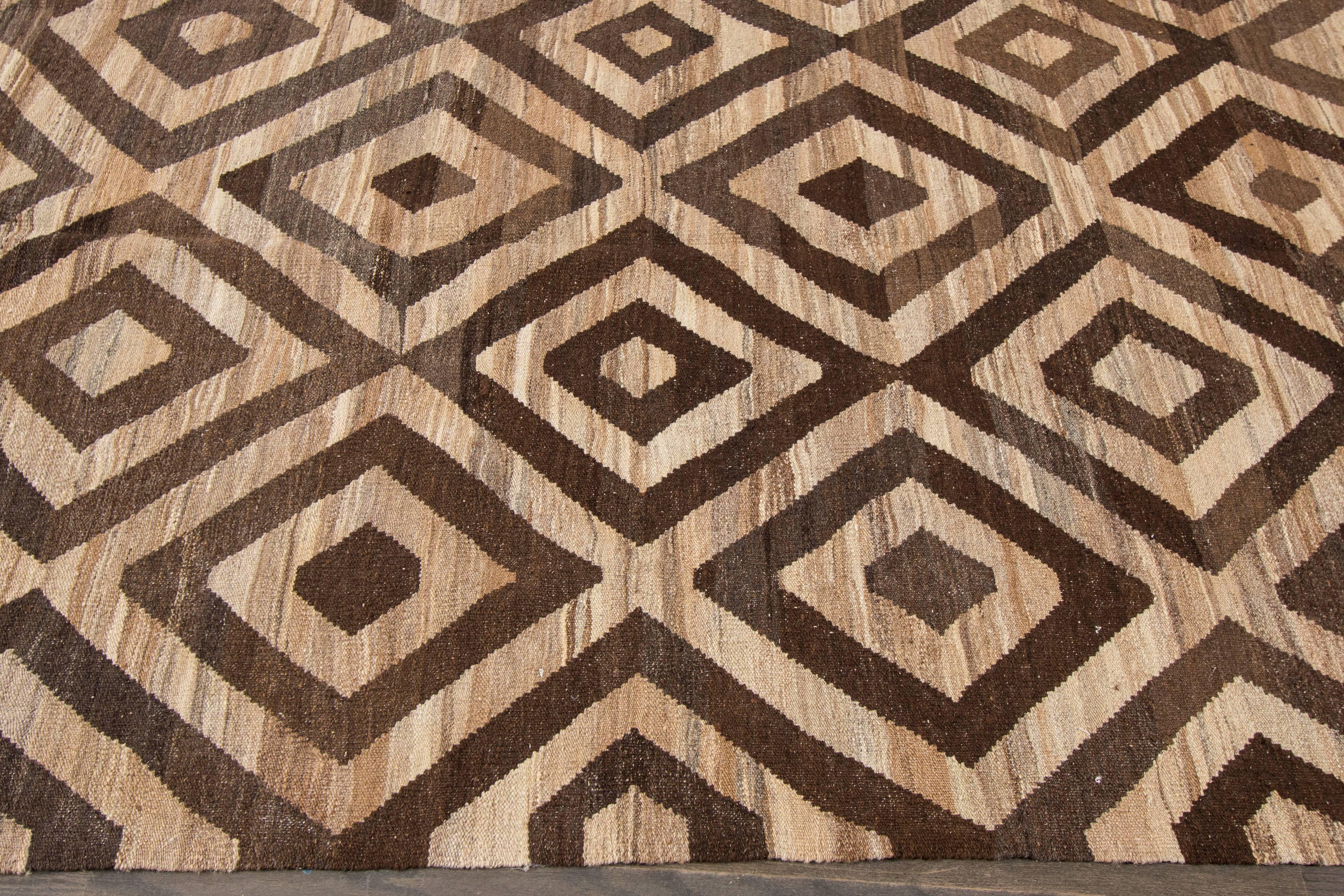 A hand-knotted Kilim rug with a geometric design on a brown field. Accents of dark brown and ivory throughout the piece. This rug measures 8'.6 x 9'.11.