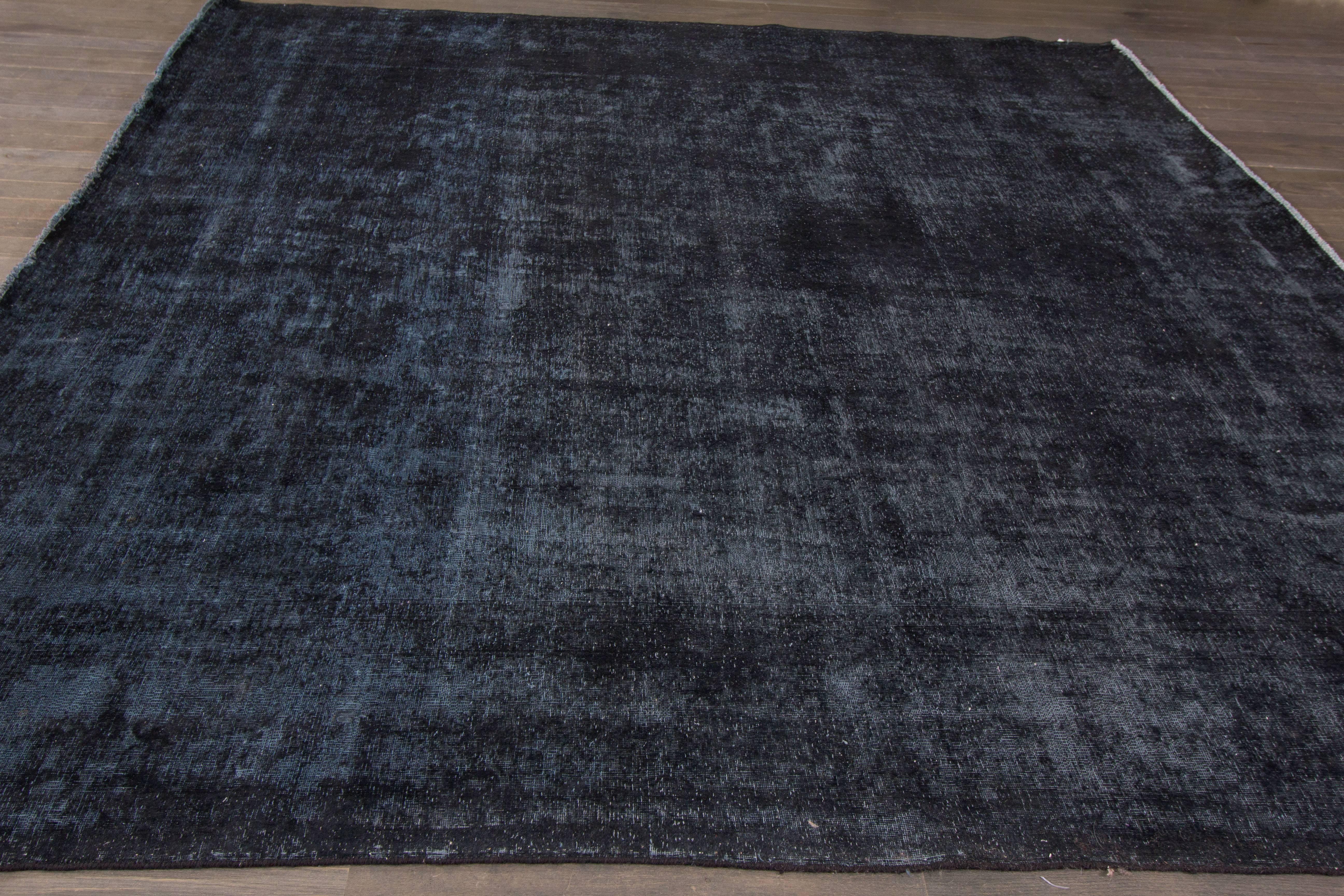 A hand-knotted square overdyed rug with an all-over design on a dark blue field. Accents of ivory and blue throughout the piece. This rug measures 9'.4 x 9'.9.