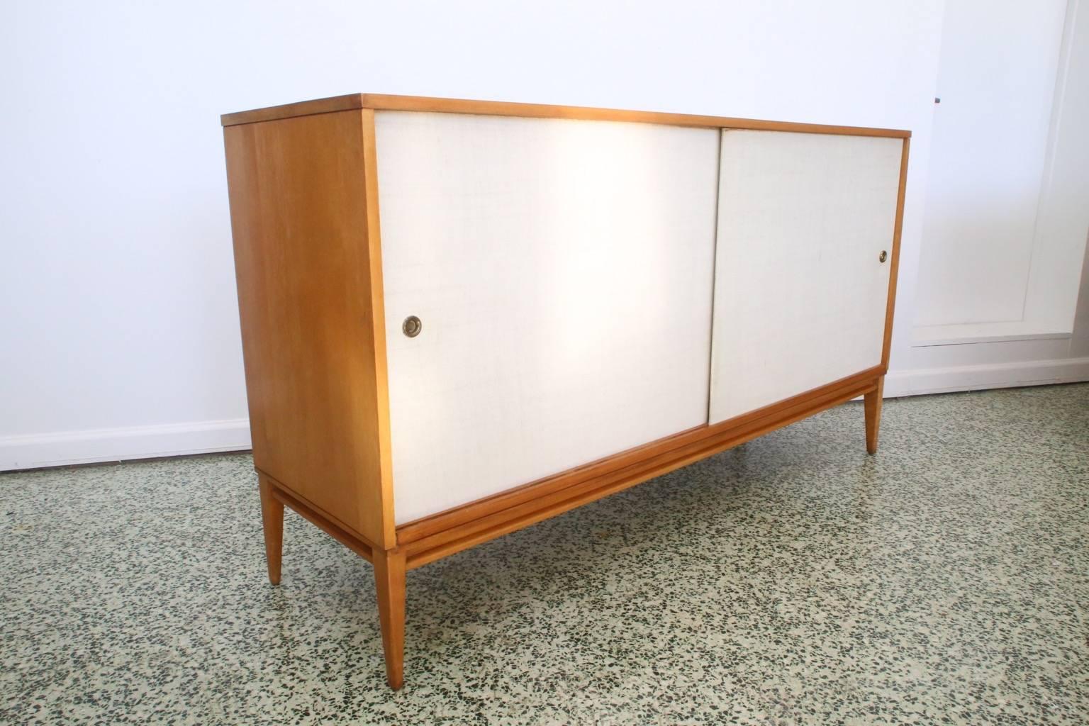 Very nice credenza with grass cloth doors with adjustable shelves and drawers designed by Paul McCobb for Winchendon. We have smaller companion piece listed separately on 1stdibs.