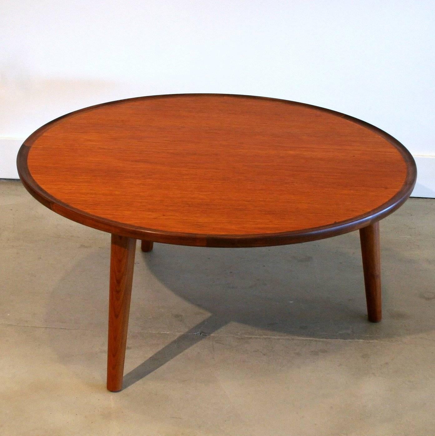 Beautiful teak coffee table by Peter Hvidt. Large top surface with solid old growth teak lip. Resting on three solid teak splayed legs.