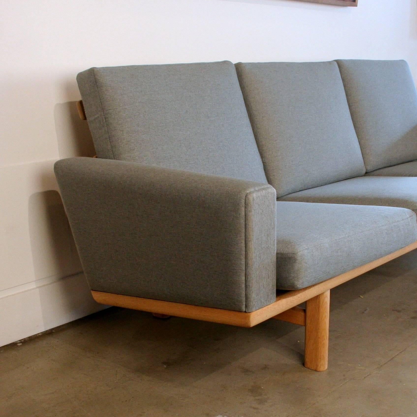 Recently reupholstered in a warm grey fabric, this solid oak iconic model GE-236 sofa by Hans Wegner is a showstopper in any space. Float the sofa in a space to show the sculptural legs and back details.