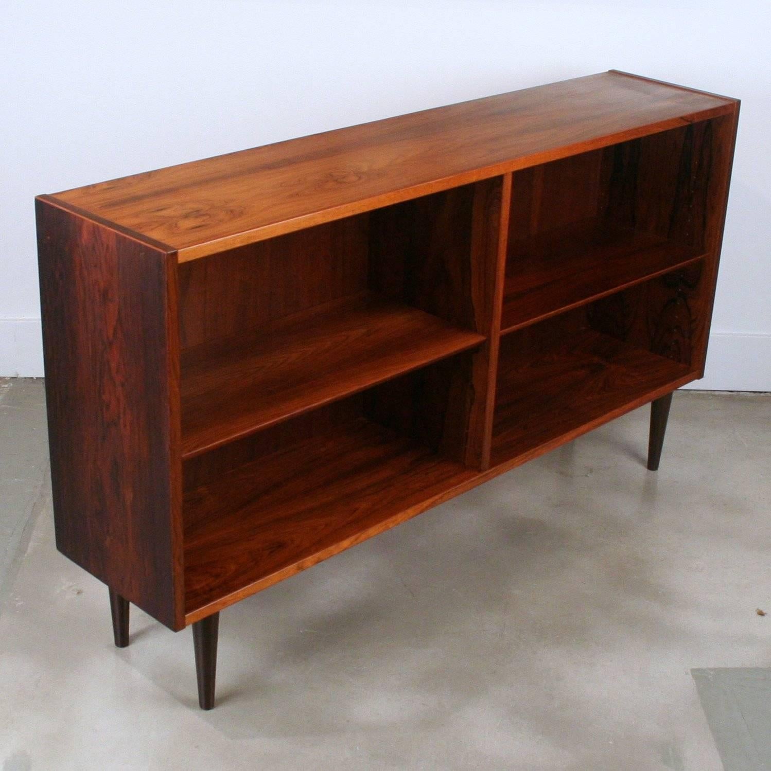 Lovely low-profile bookcase crafted in rosewood sitting on conical wood legs, width adjustable shelving.