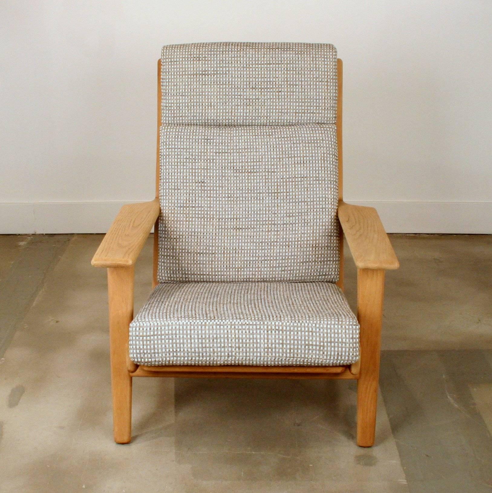 Exquisite vintage highback lounge chair by Hans Wegner in solid oak. Newly reupholstered in a grey tweed. Features high headrest, splayed legs and wide armrests. Made in Denmark.