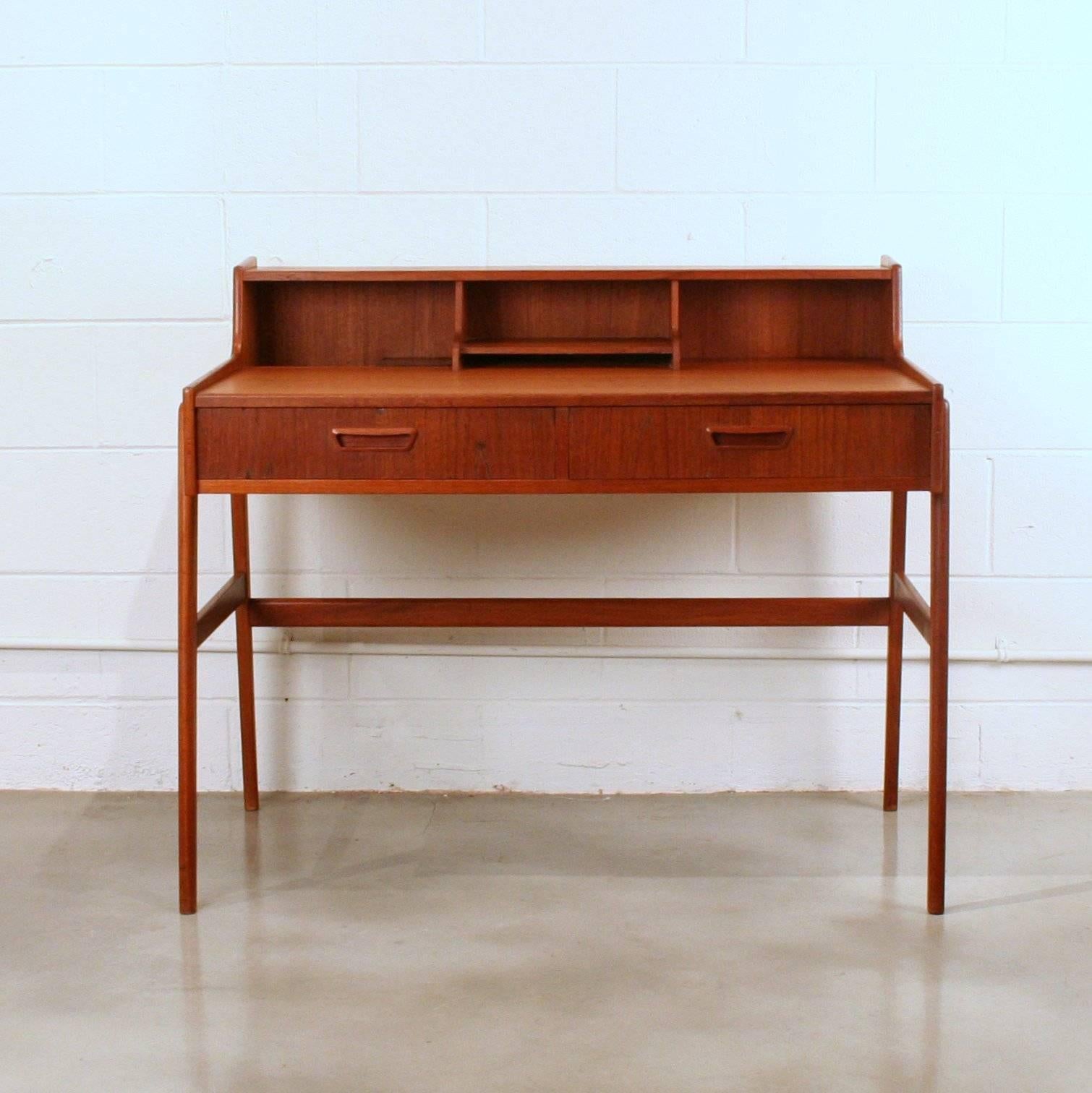 Delightful vintage teak writing desk featuring two drawers with inset finger pulls. Desk also features small storage compartments on desk top. Set on solid teak, flowing legs. Made in Denmark.