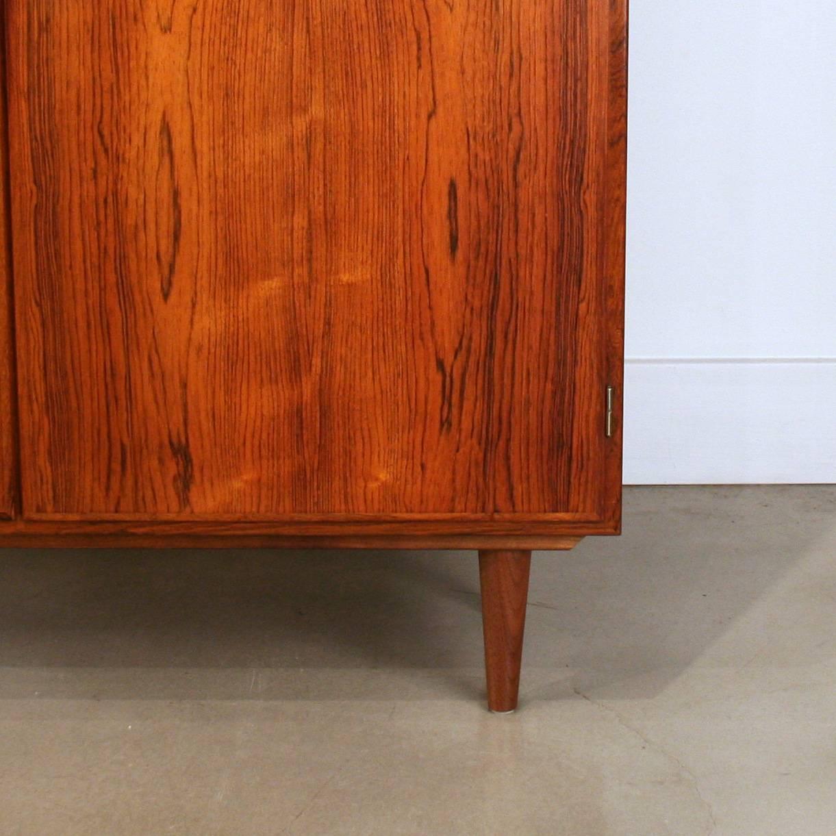 Stunning tall rosewood cabinet with solid rosewood pulls. Resting on short, solid conical legs. Interior opens with four adjustable shelves. Working original lock. Made in Denmark.