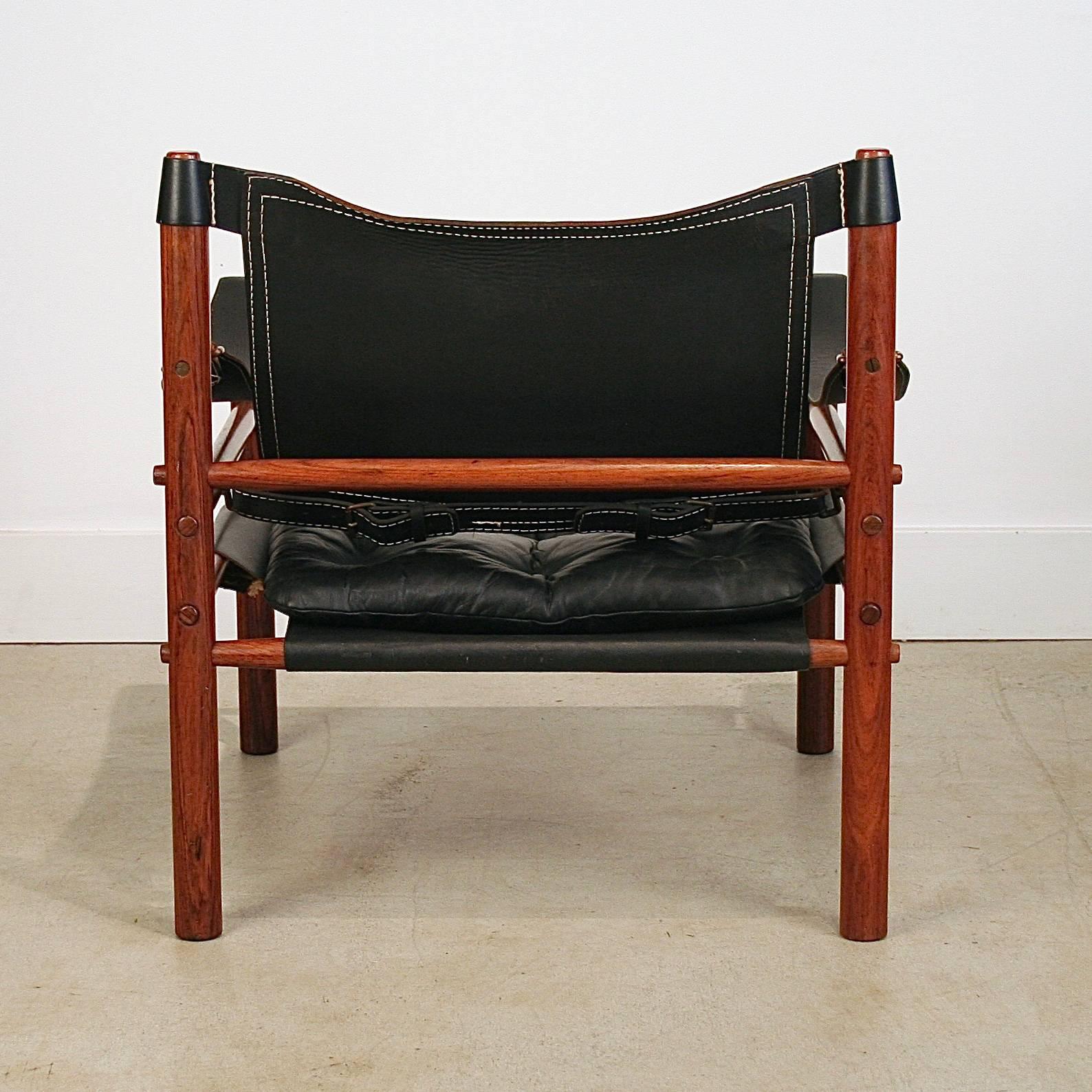Beautiful Sirocco lounge chair by Arne Norell. Rosewood frame and black leather upholstery, with a removable cushion. Great details of wood plugs decorating the screw holes, seams in the leather and brass buckles. Made in Denmark.