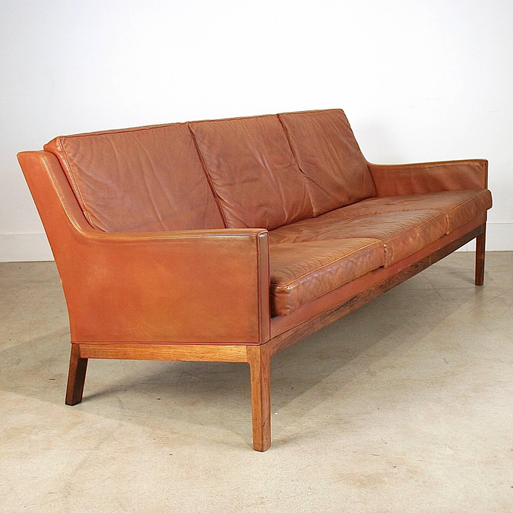 Beautiful vintage Danish leather three-seat sofa on rosewood base. Three loose seat back cushions over three loose seat cushions. Wonderful 1960s modern piece. Made in Denmark.