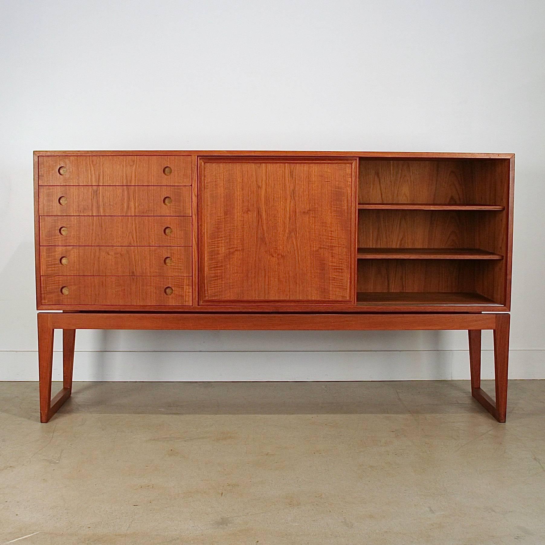 Stunning vintage Danish teak sideboard. Features five drawers with dovetail joinery and circular inset pulls on each drawer. Two sliding doors with beautifully crafted pull details surround each door. Sliding doors open onto storage space with two