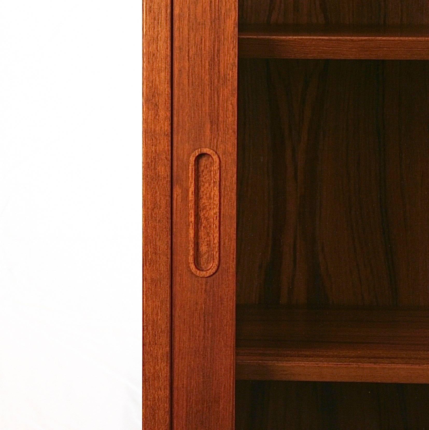 Beautiful vintage Danish teak and glass cabinet. This piece features sliding doors with wonderfully crafted finger pulls and adjustable shelves. This cabinet has an unfinished back. Made in Denmark.
 