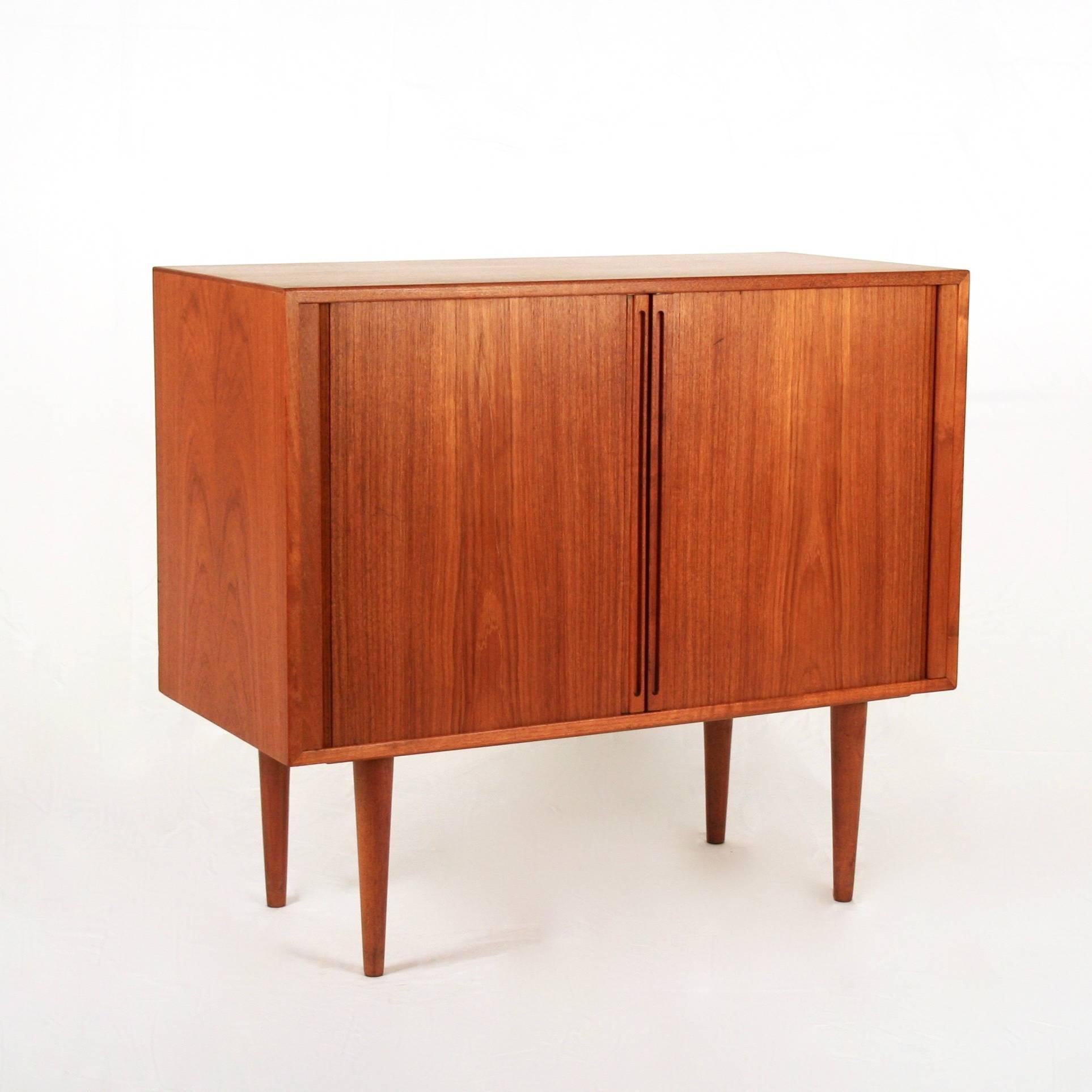 A lovely small-scale cabinet with warm teak patina and tambour doors that slide out of sight. With conical legs and a clean design, this piece is a great storage solution for media or anything else you desire. Designed by world renowned Danish