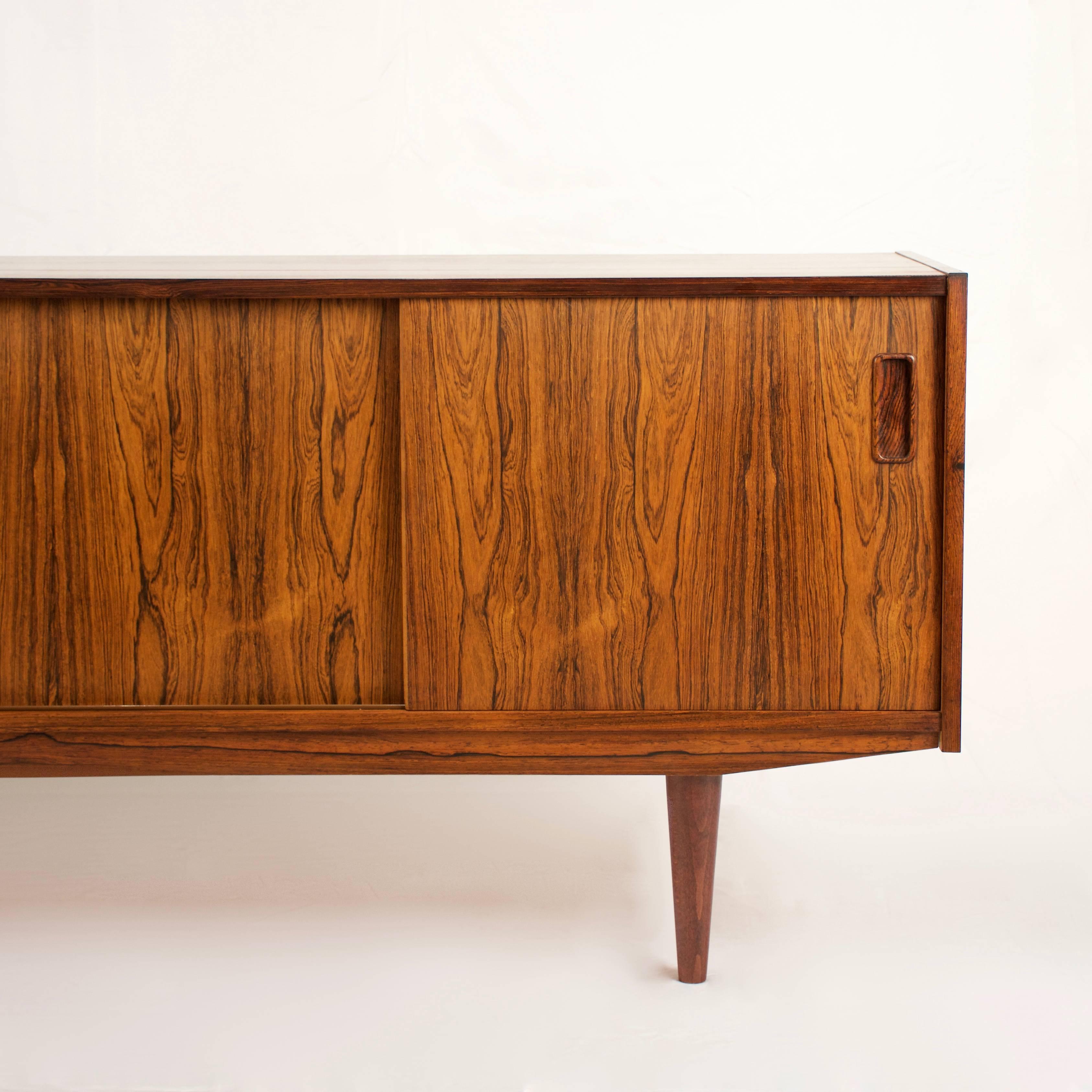 Beautiful vintage Danish rosewood sideboard. This piece features four sliding doors with inset rectangular pulls. These doors open onto a storage space with adjustable shelves and removable trays. Made in Denmark.