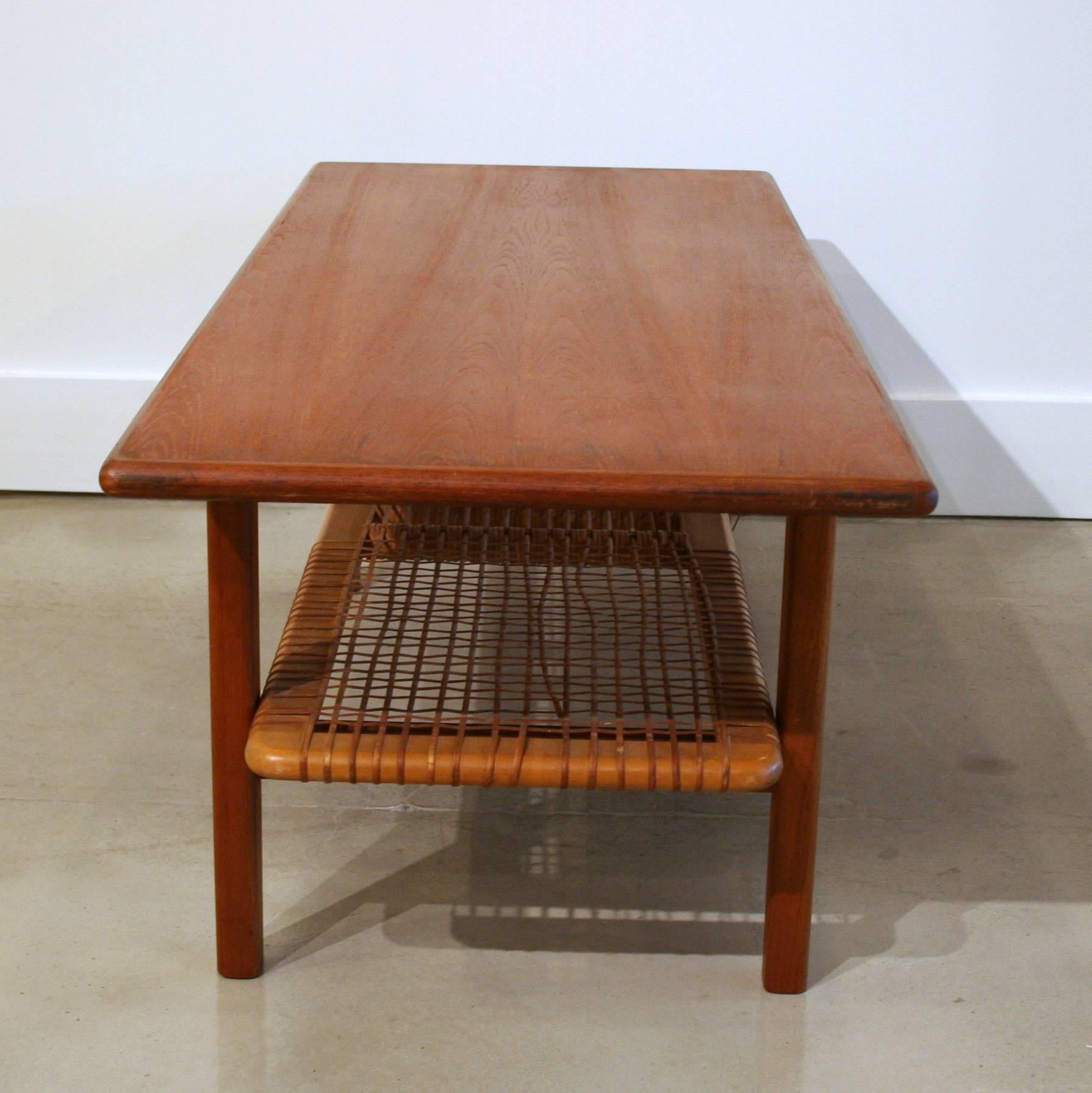 Solid teak coffee table with rounded edges and a lower shelf with caning. Sleek, and simple, full of mid-century character.