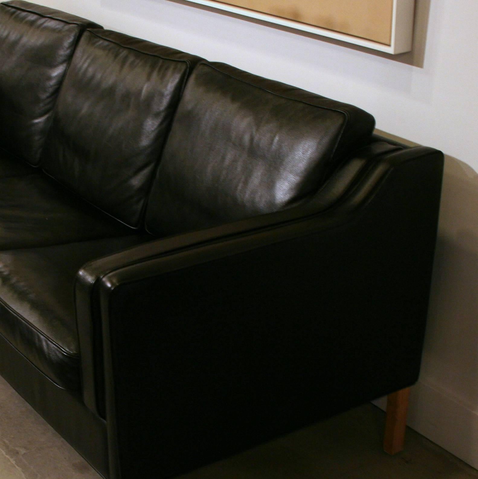 Supple full-grain black leather covers this sleek design modelled after the Classic Børge Mogensen sofa designs of the 1950s and 1960s. This vintage piece features the signature sloped arms with piping detail, and the loose cushions are filled with