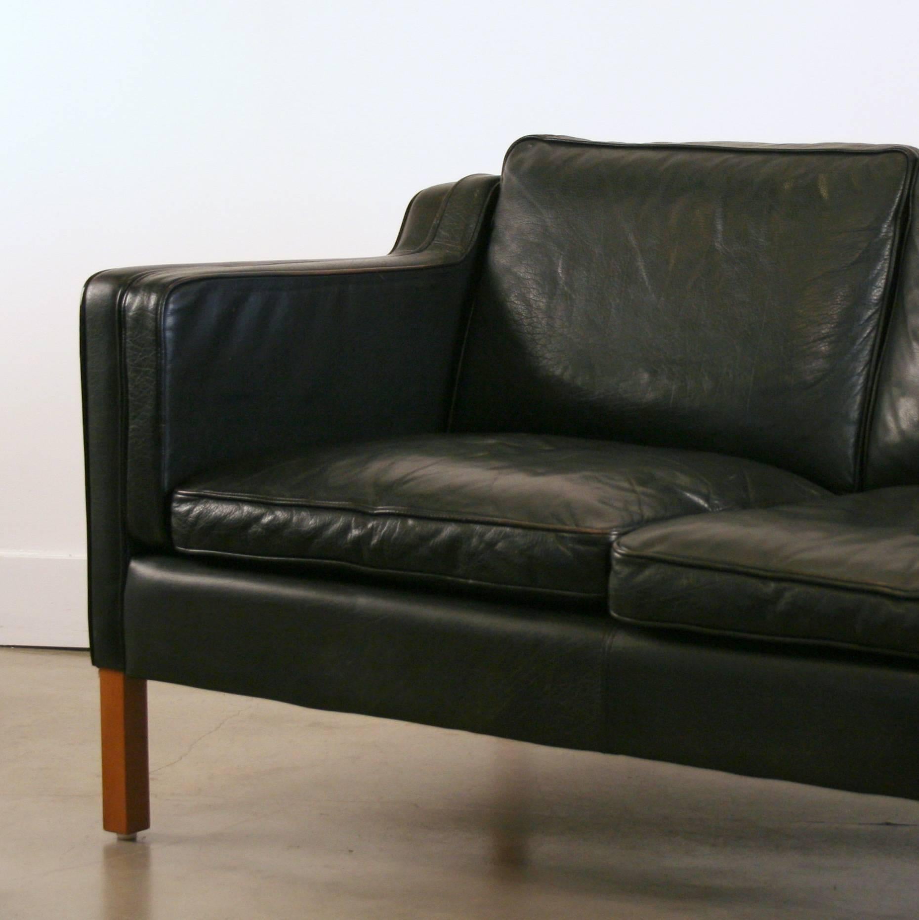 Supple full-grain black leather covers this sleek design modeled after the Classic Borge Mogensen sofa designs of the 1950s and 1960s. This vintage piece features the signature sloped arms with piping detail, and the loose cushions are filled with a