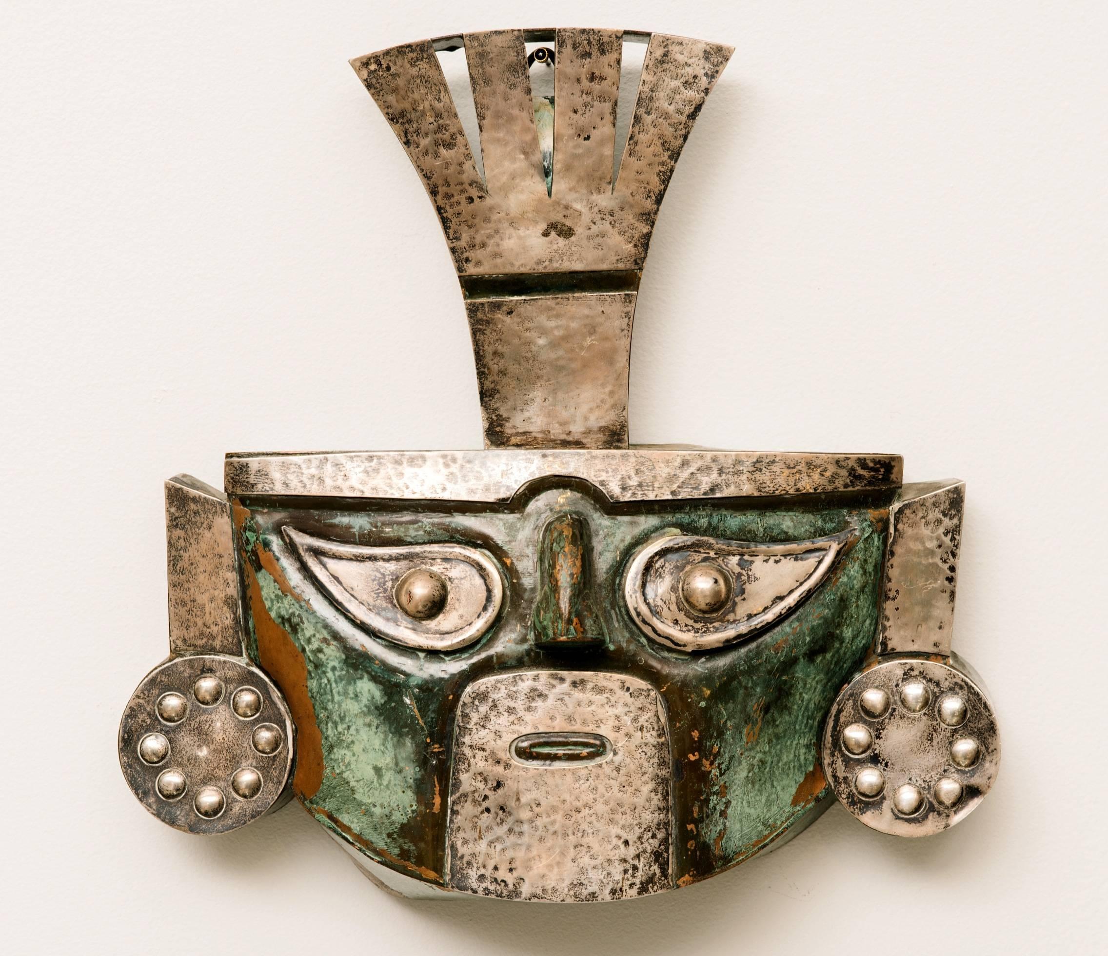 A rare pair of Peruvian masks  attributed to Graziella Laffi. The large green one made of copper and brass has a commanding Pre-Columbian Moche image surrounded by dragons on either side while the smaller one is mostly silver with a small amount of