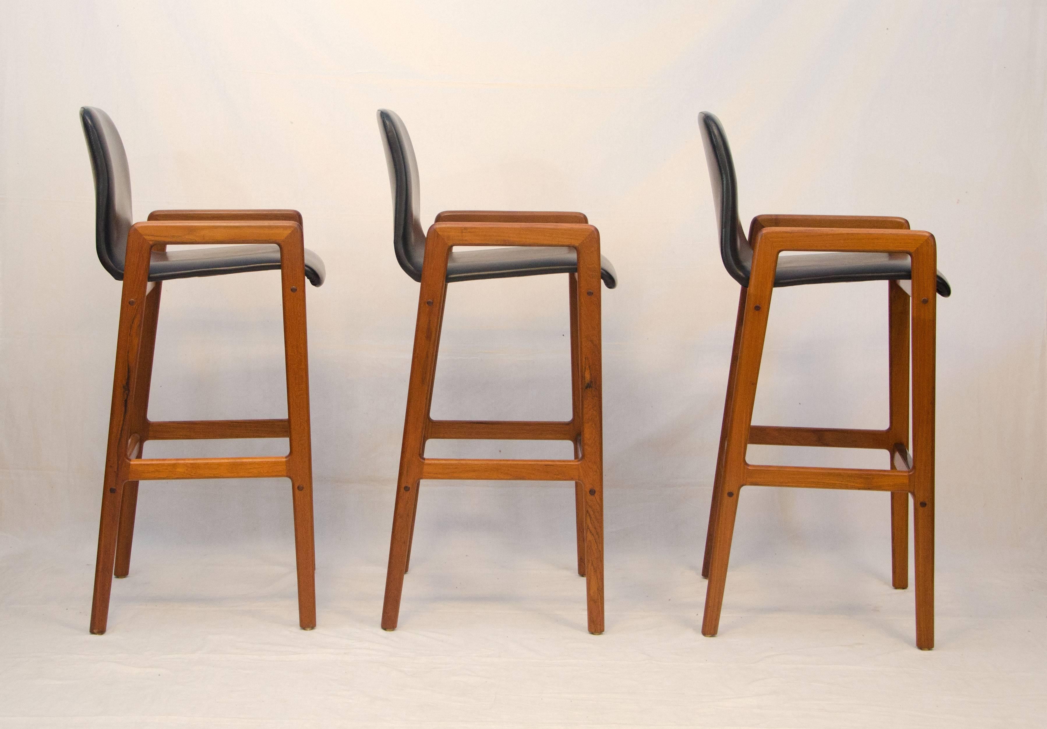 Comfortable Danish teak counter or bar stools. Manufactured tags on seat bottoms: Tarm Stole OG Mobelfabrik. All three foot rests are protected by a formica strip so the wood does not get damaged with use. Seating space between the arms is 17