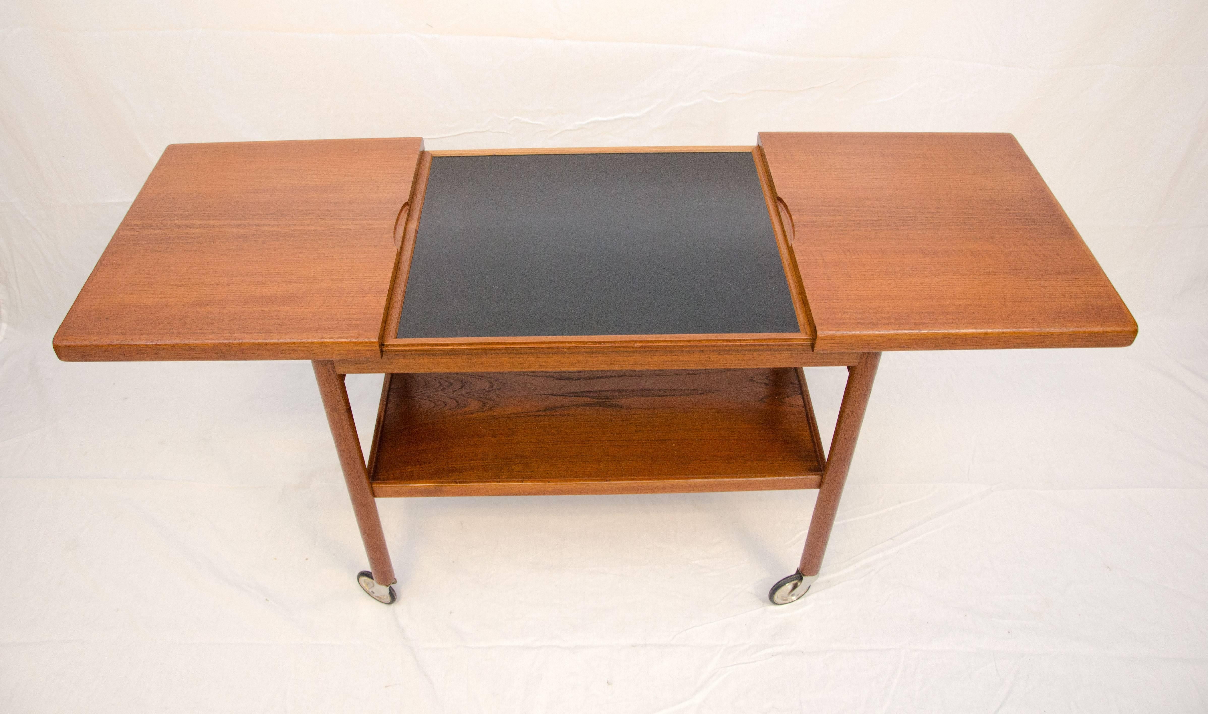 Very nice Danish teak rolling bar or serving cart, attributed to Arne Vodder. The top surface pulls apart at both ends to 51" wide to reveal a black Formica mixing surface, which would be water resistant or would be good for placement of warm