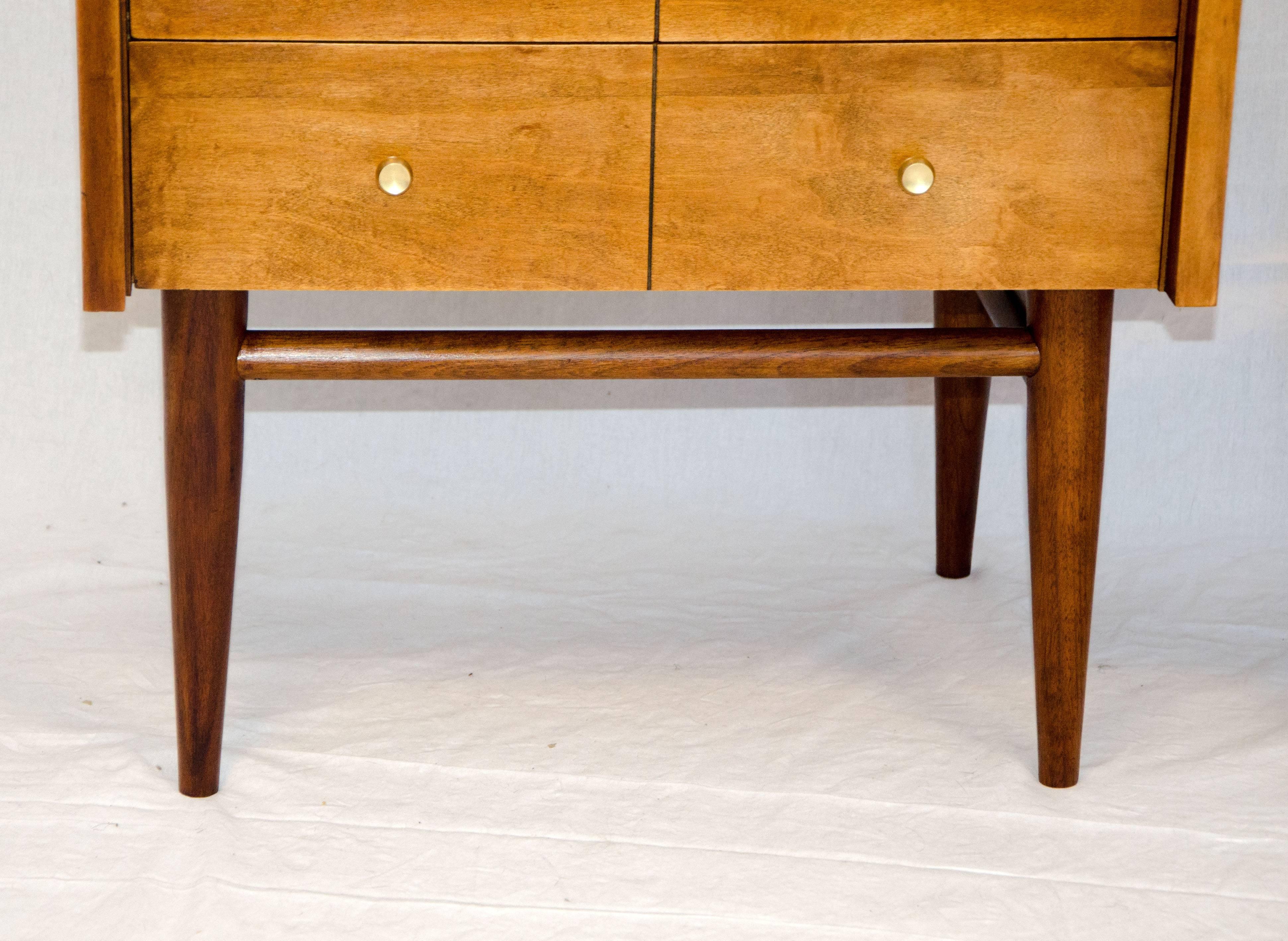 Very nice pair of nightstands with walnut bases and birch cabinets. Finished in a teak or light walnut color. Original brass drawer pulls remain on all four drawers. Company logo remains in top drawer of both nightstands, from the 