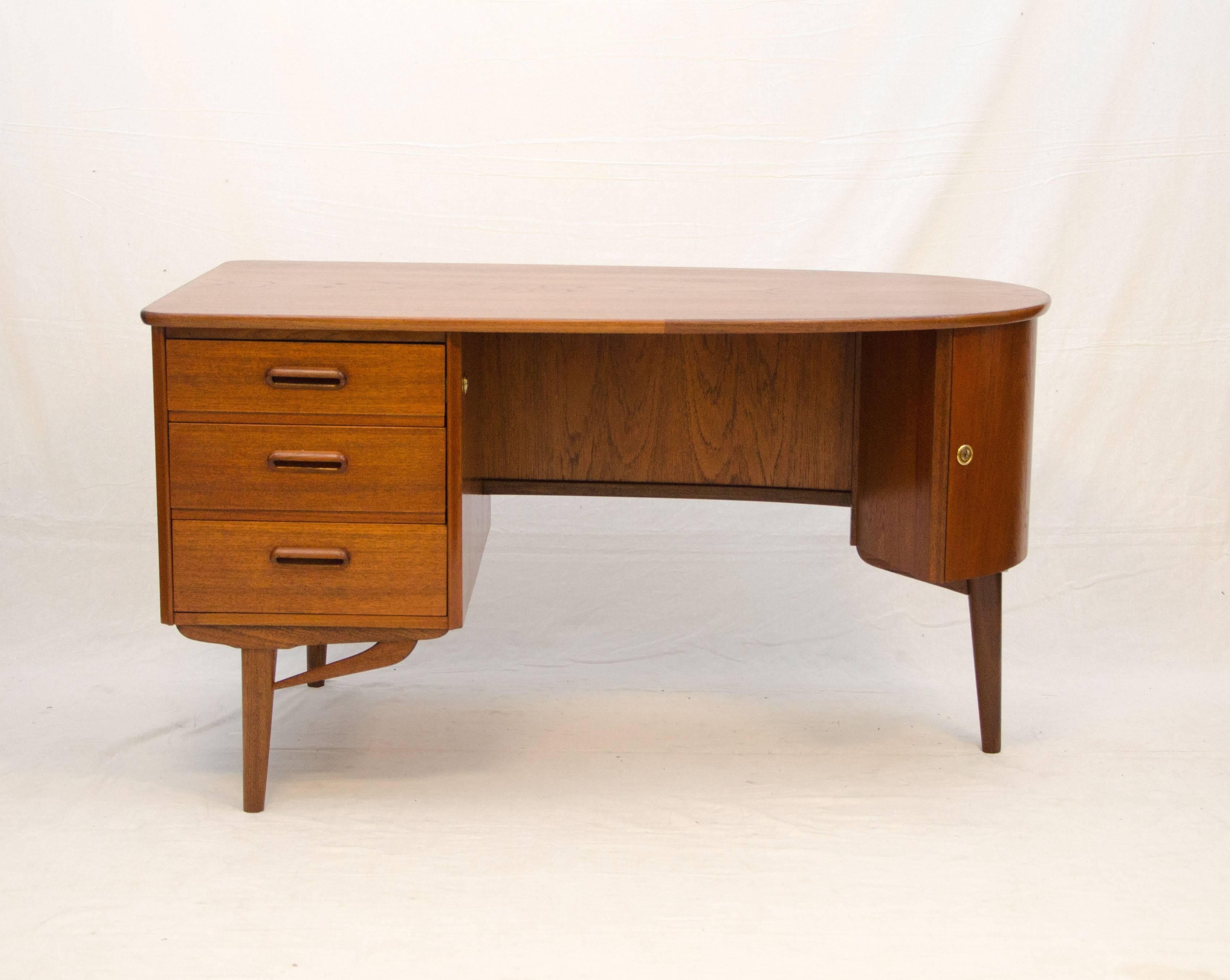 Nice medium size Danish Mid-Century Modern teak desk with an elliptical top and several features. There is a set of storage drawers on the left side and a curved storage cabinet with a small shelf on the right side. At the back there is a bookshelf
